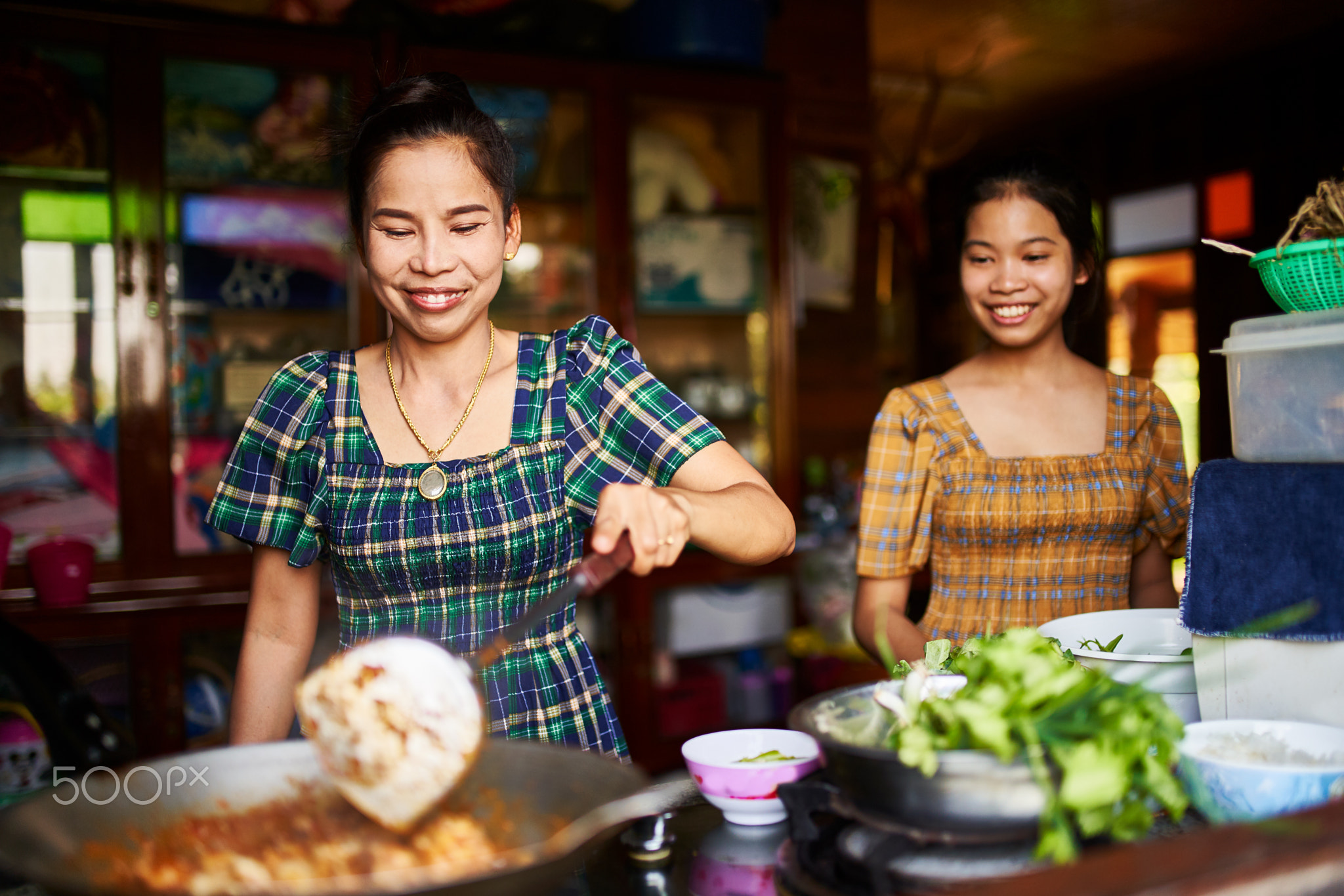 thai mother and daughter cooking together in rustic kitchen makign red curry