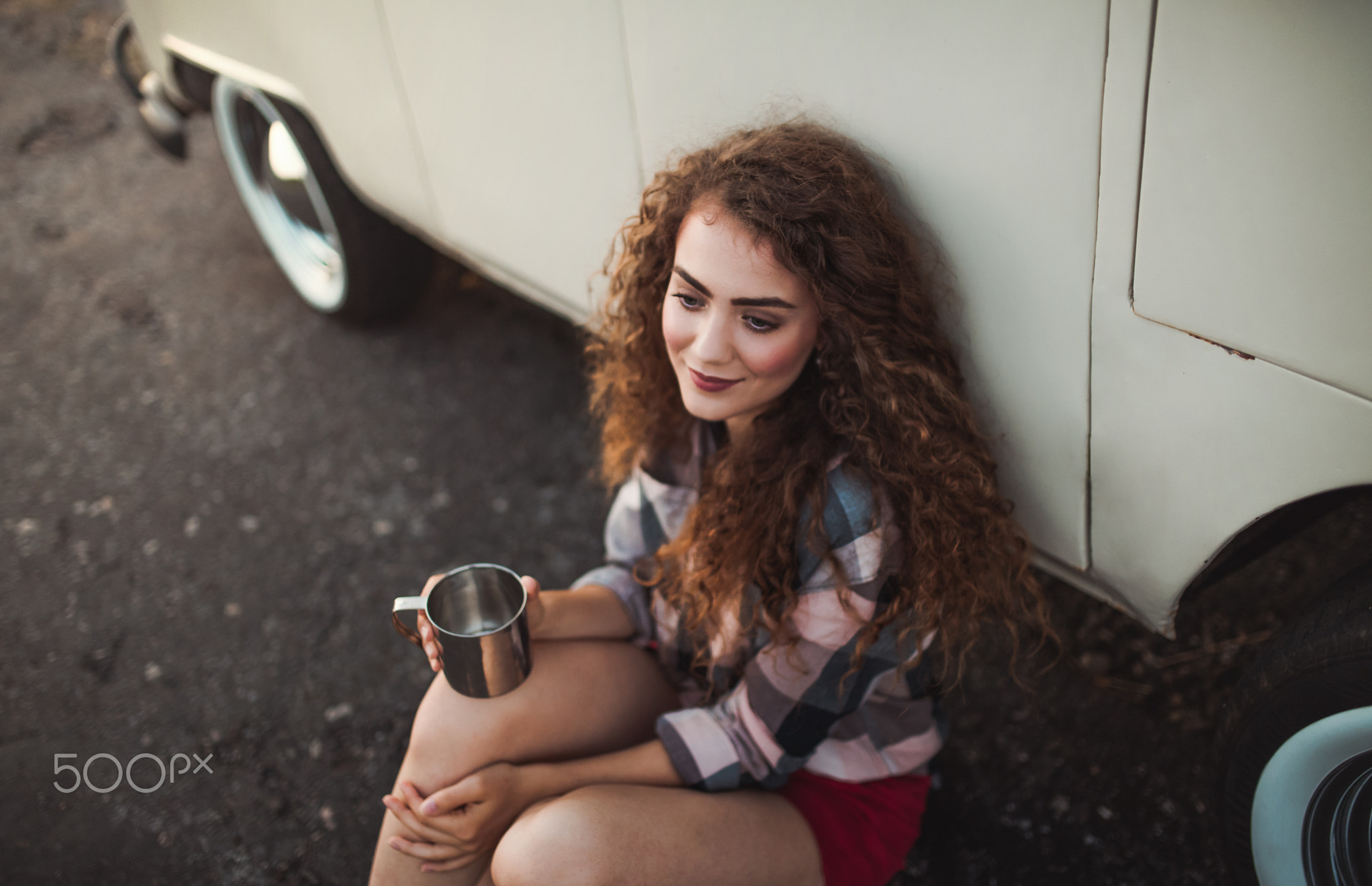 A young girl sitting by a car on a roadtrip through countryside.