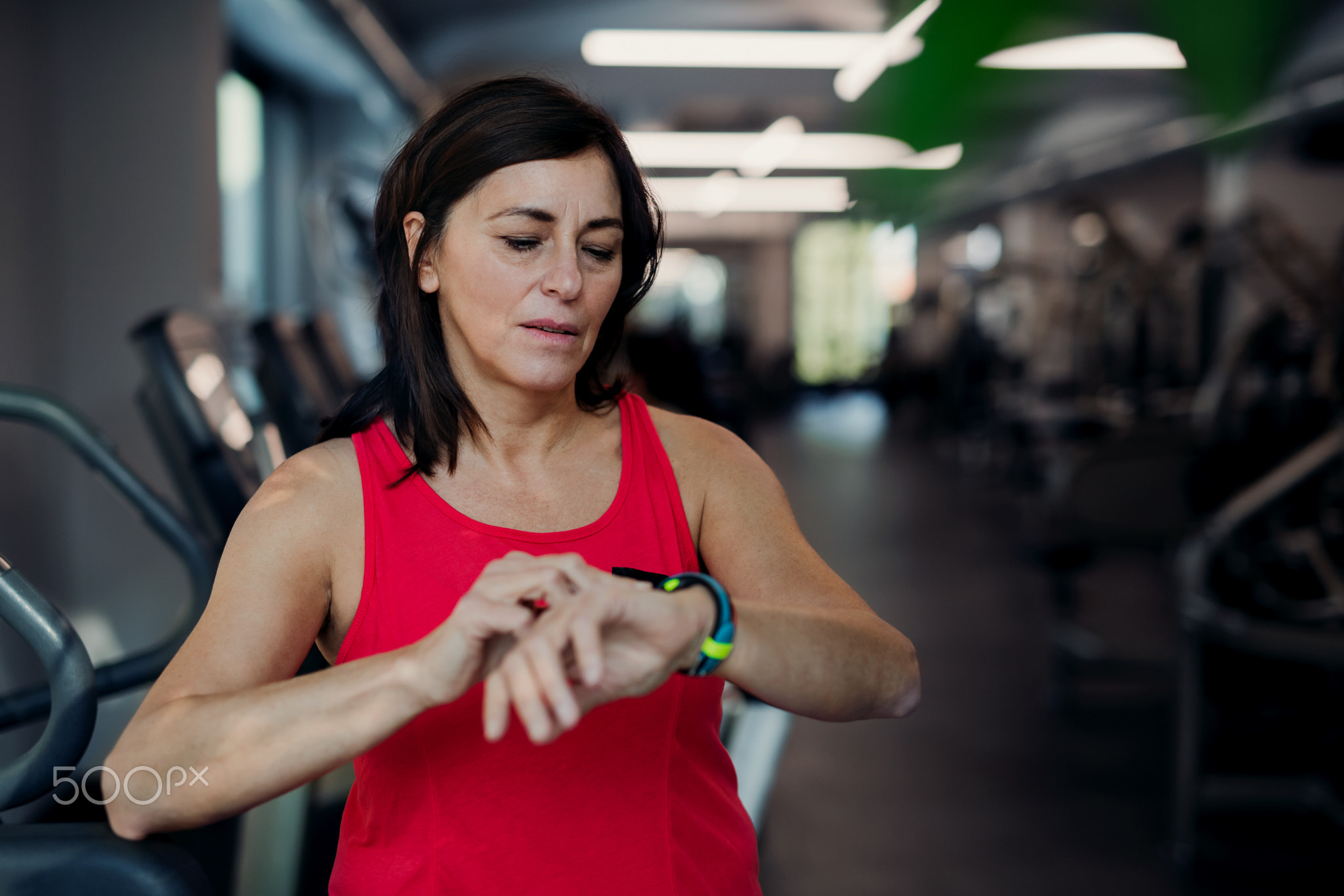 A senior woman in gym resting after doing exercise, checking time.