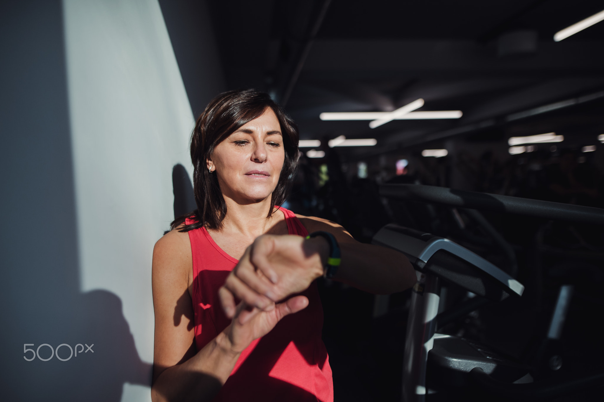 A senior woman in gym resting after doing exercise, checking time.