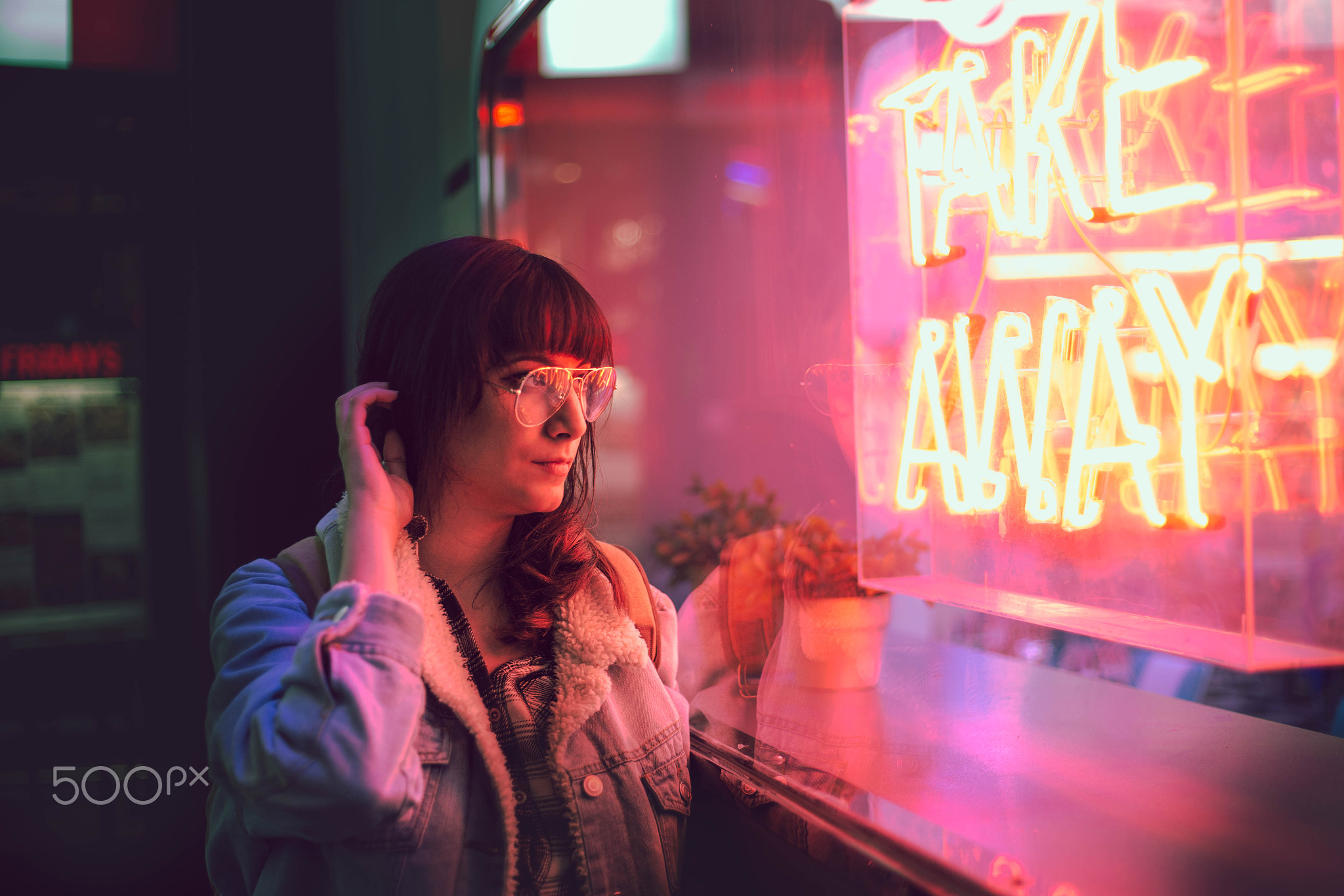 young woman touching her hair looking through the glass next to a club with a window with neon...
