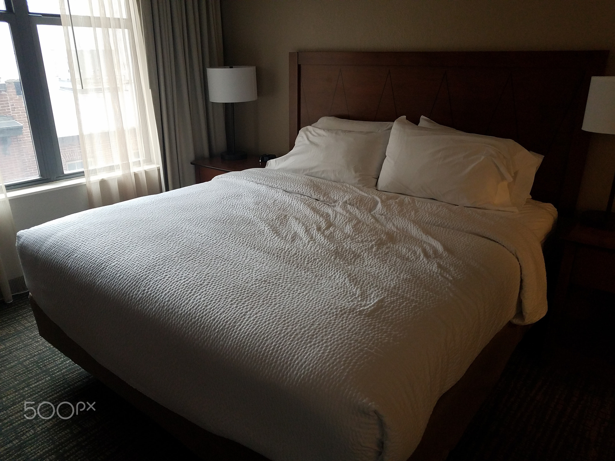 bed in room with white covers and lights and window