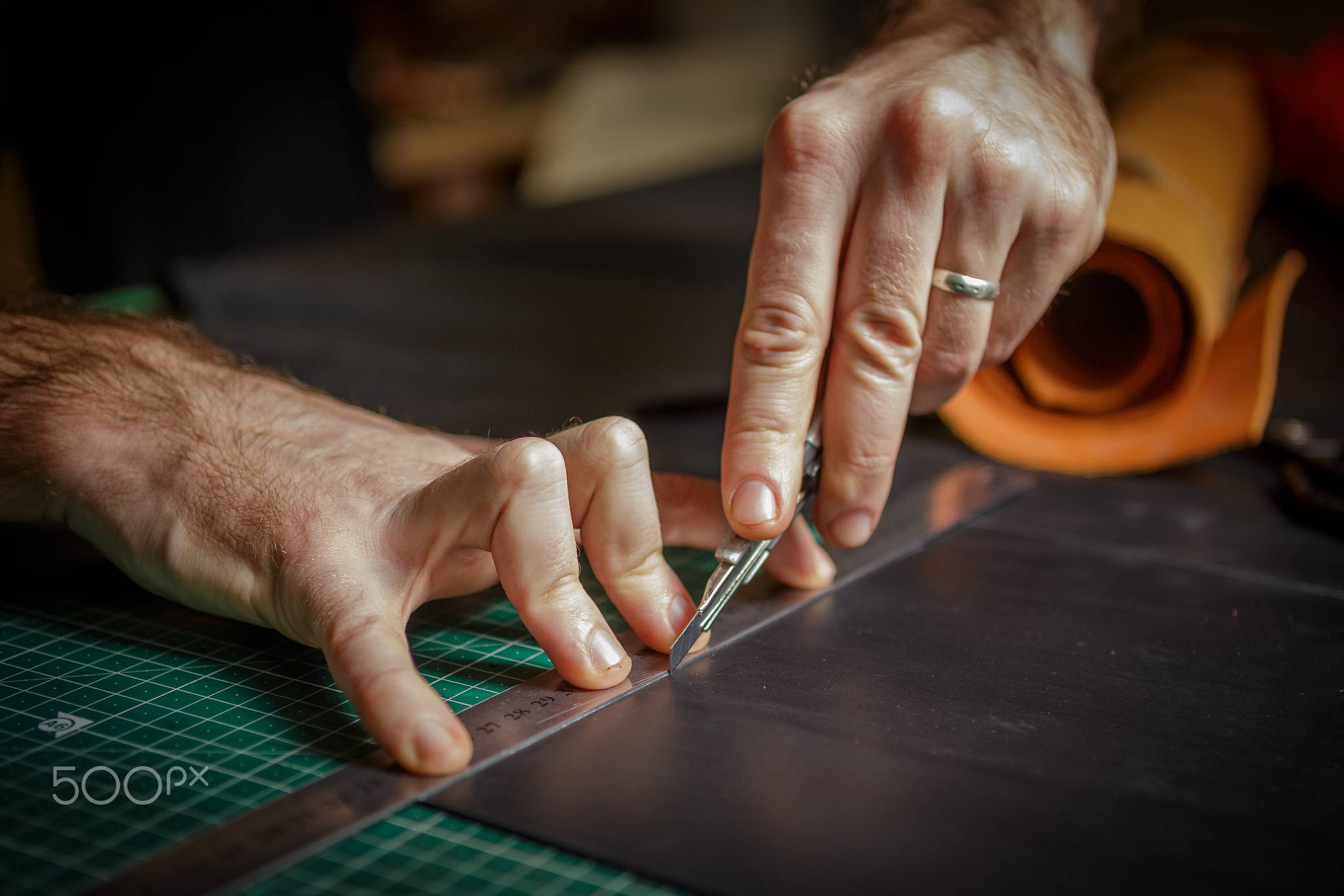 man working as artisan in his leather workshop, cutting leather by knife