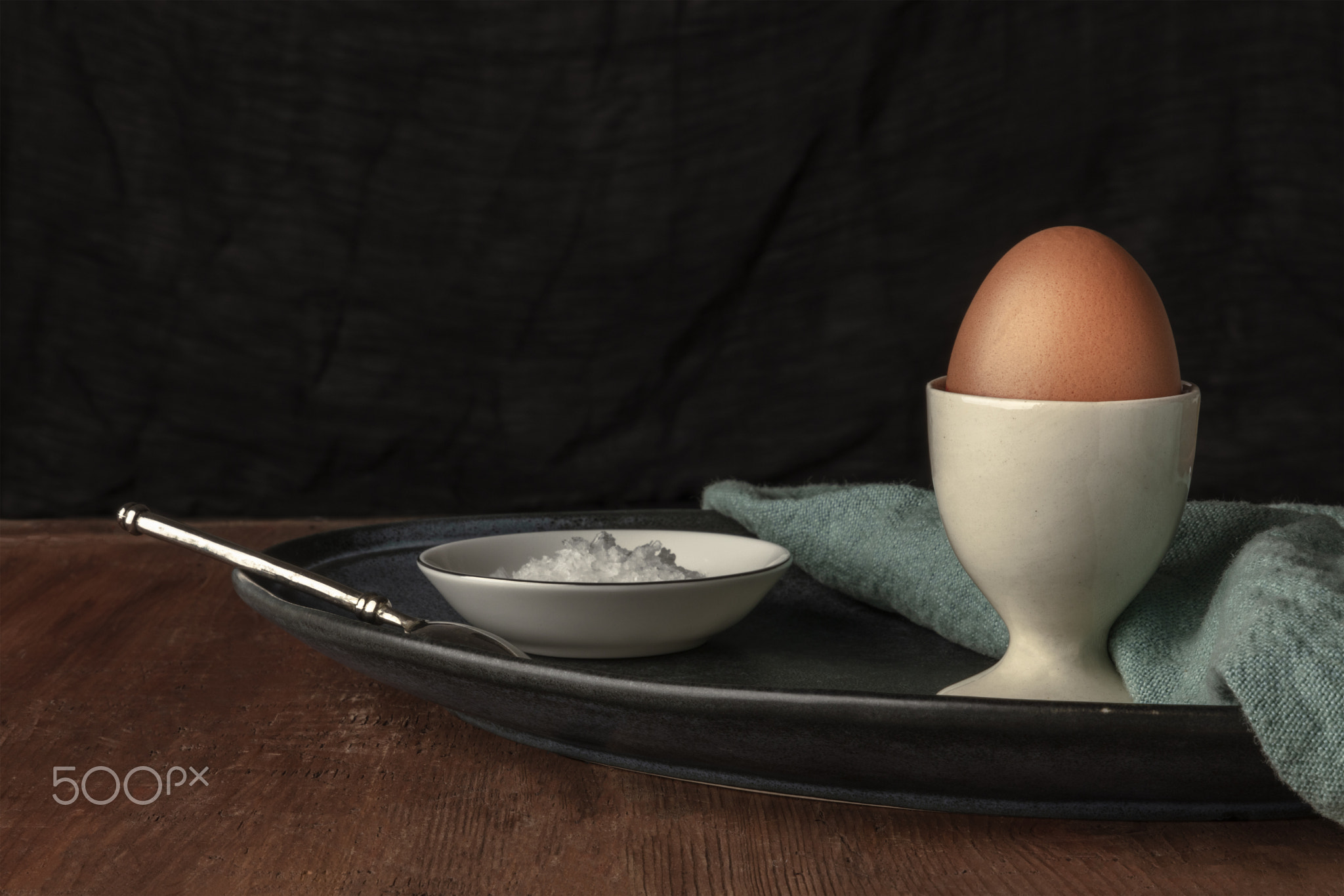 A boiled egg with salt, a side view photo on a dark background with a place for text