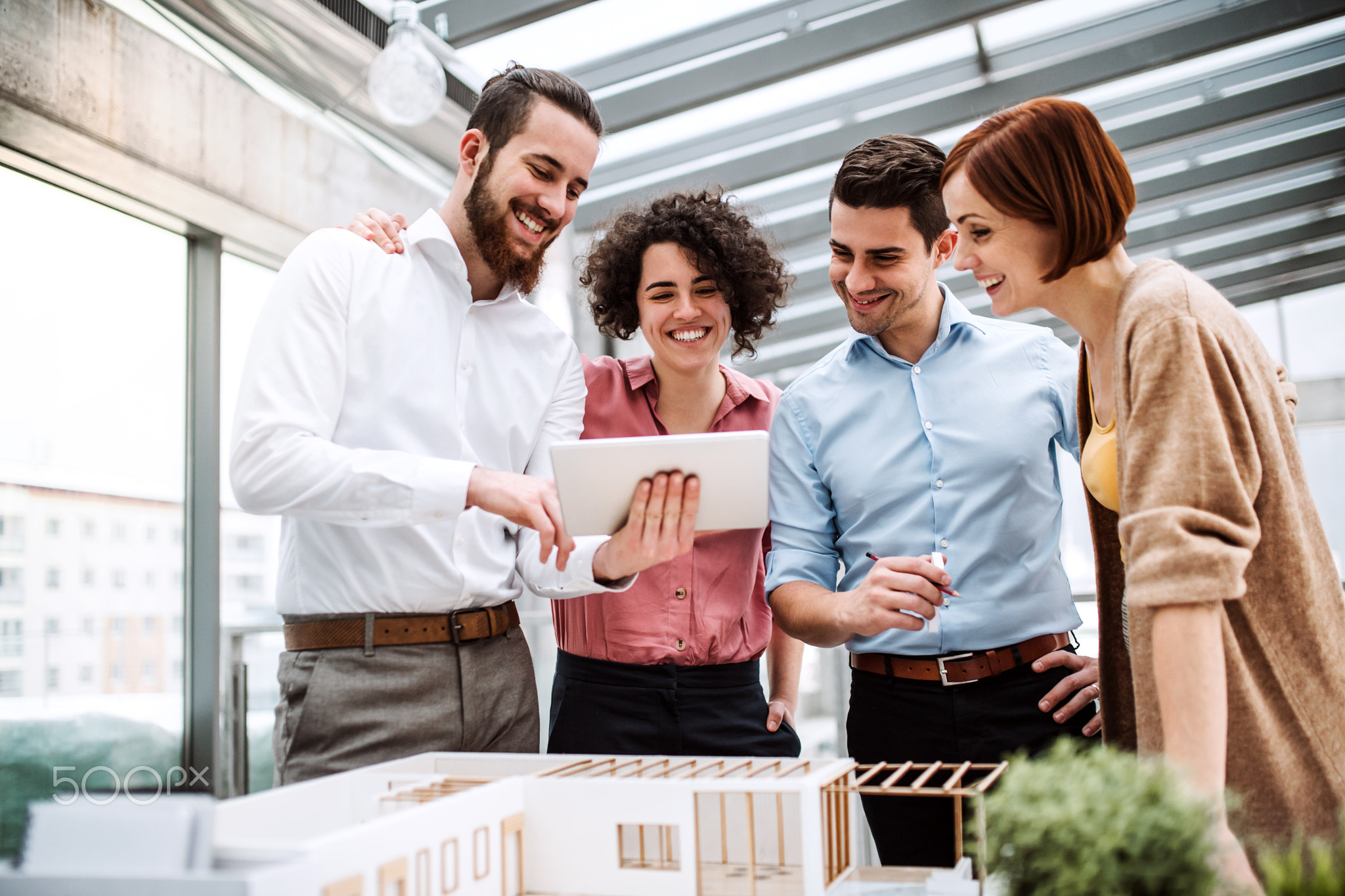 Group of young architects with tablet and model of a house standing in office, talking.