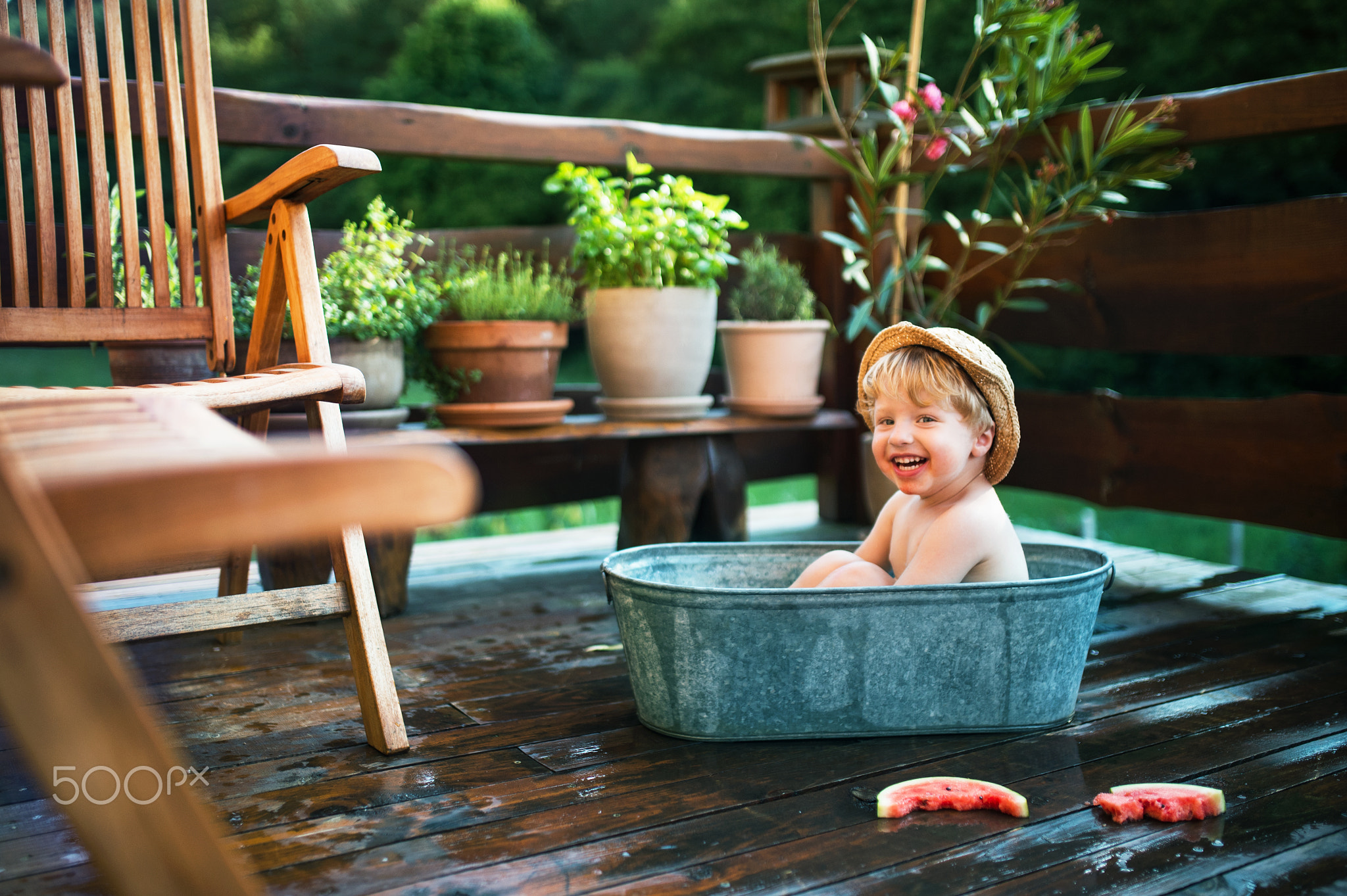 Small boy with a hat and watermelon in bath outdoors in garden in summer.