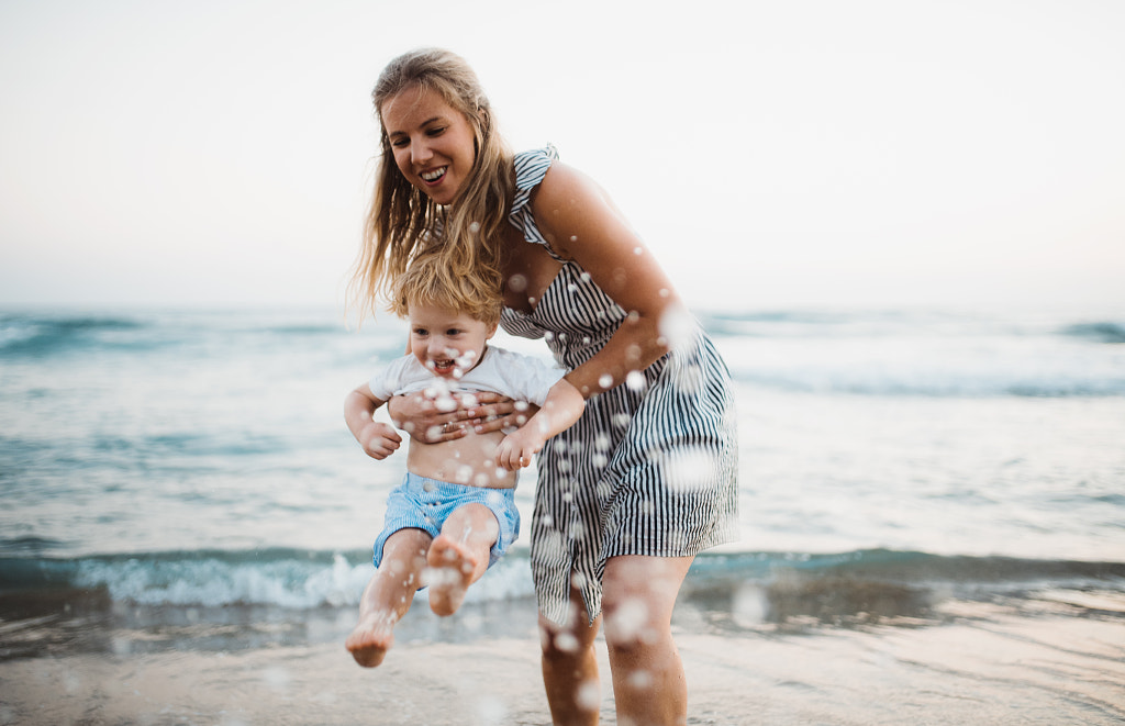 Young mother with a toddler boy standing on beach on summer holiday, having fun. by Jozef Polc on 500px.com