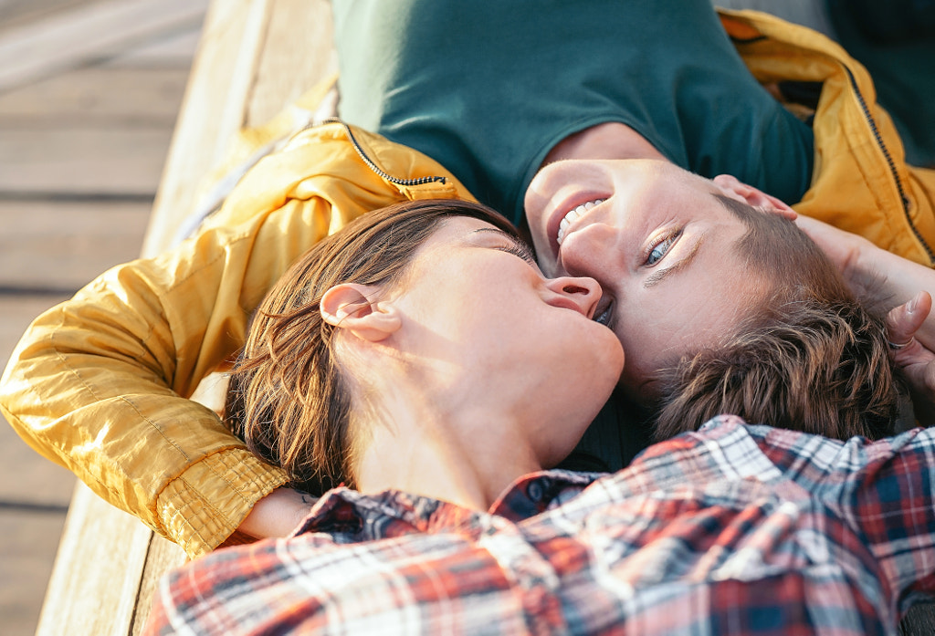 Happy gay couple lying on a bench looking each other by Alessandro Biascioli on 500px.com