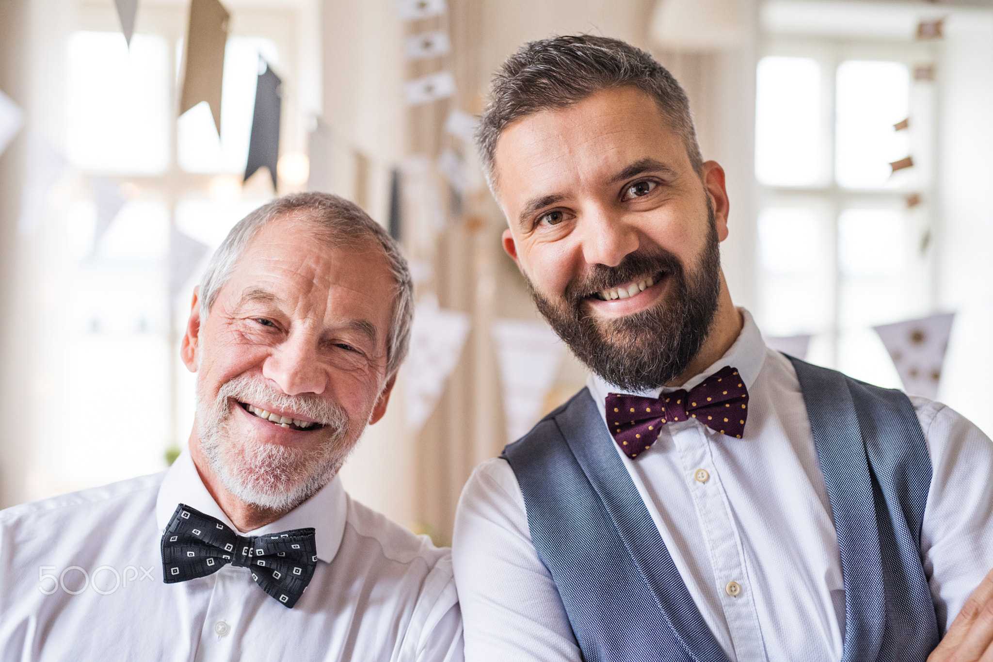 A portrait of a senior and mature man standing indoors in a room set for a party.