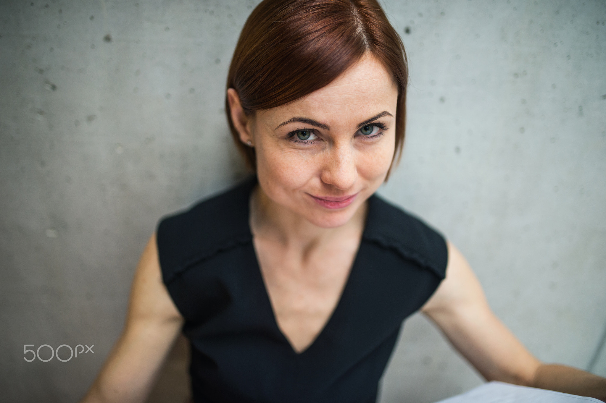 A portrait of young businesswoman standing in office, looking at camera.