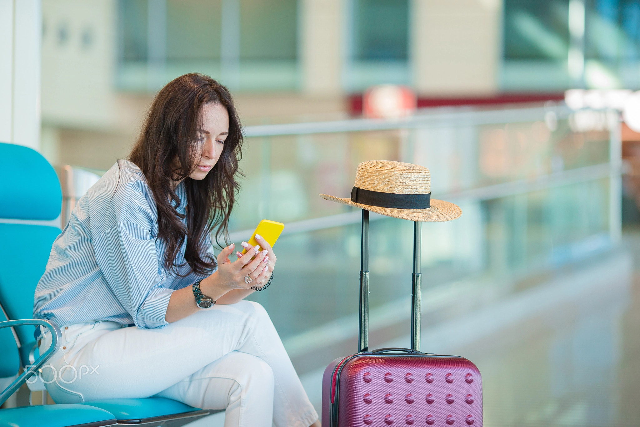 Young woman with smartphone in international airport waiting for flight aircraft