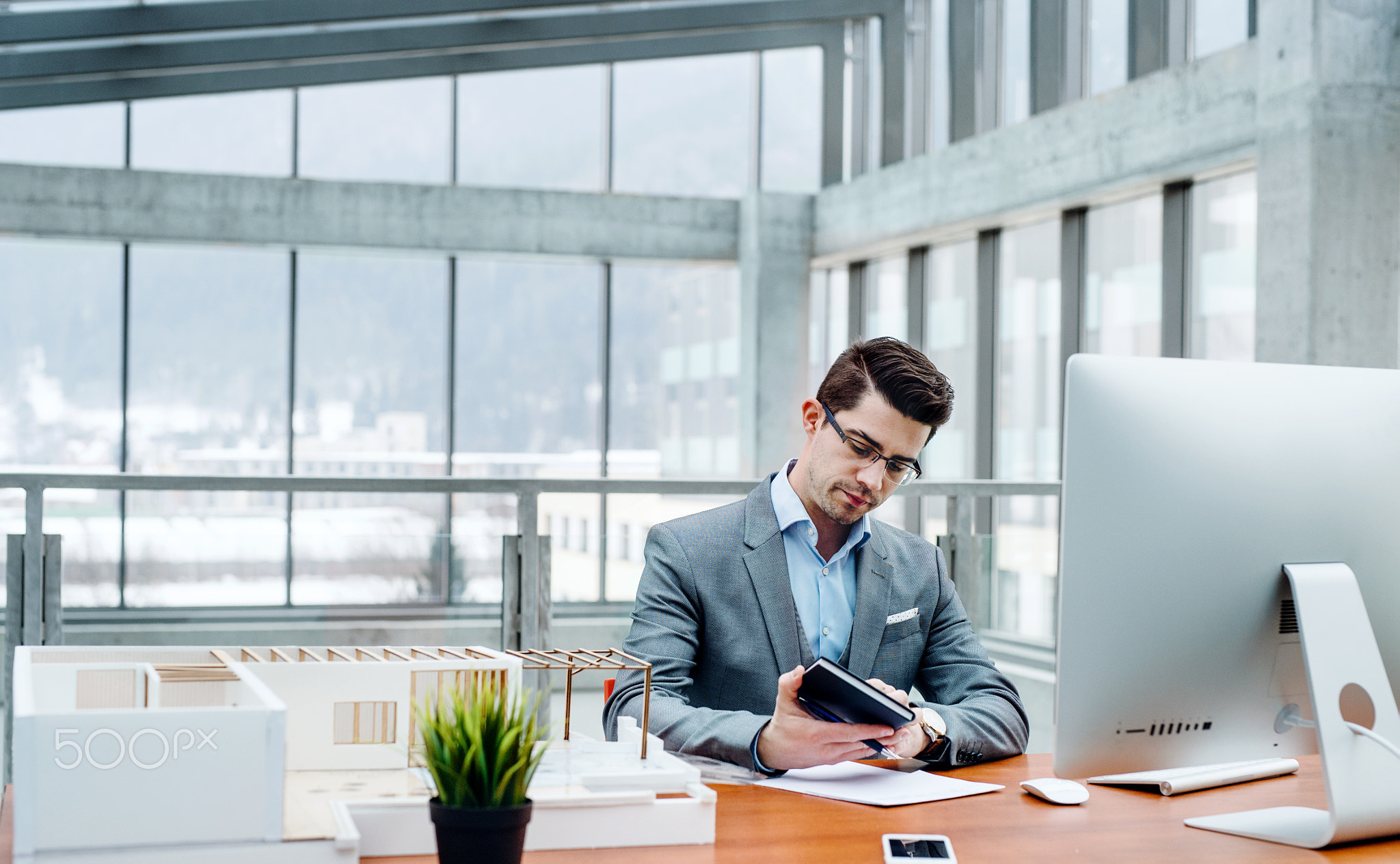 Young businessman or architect with model of a house sitting in office, working.