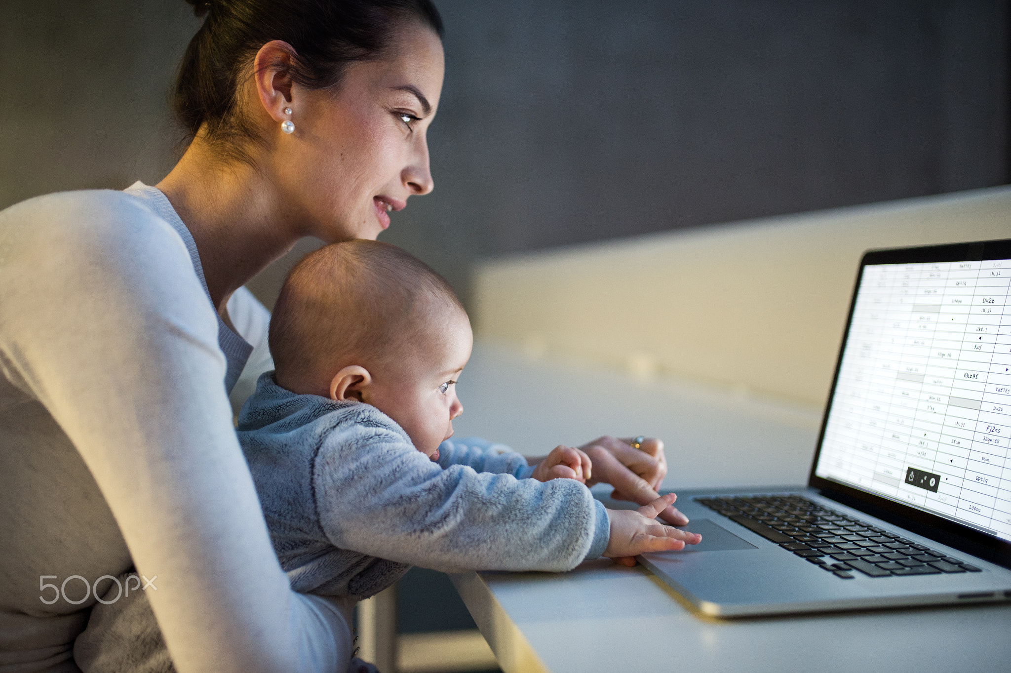 Young student with a baby sitting on desk in room in a library or office, using laptop.