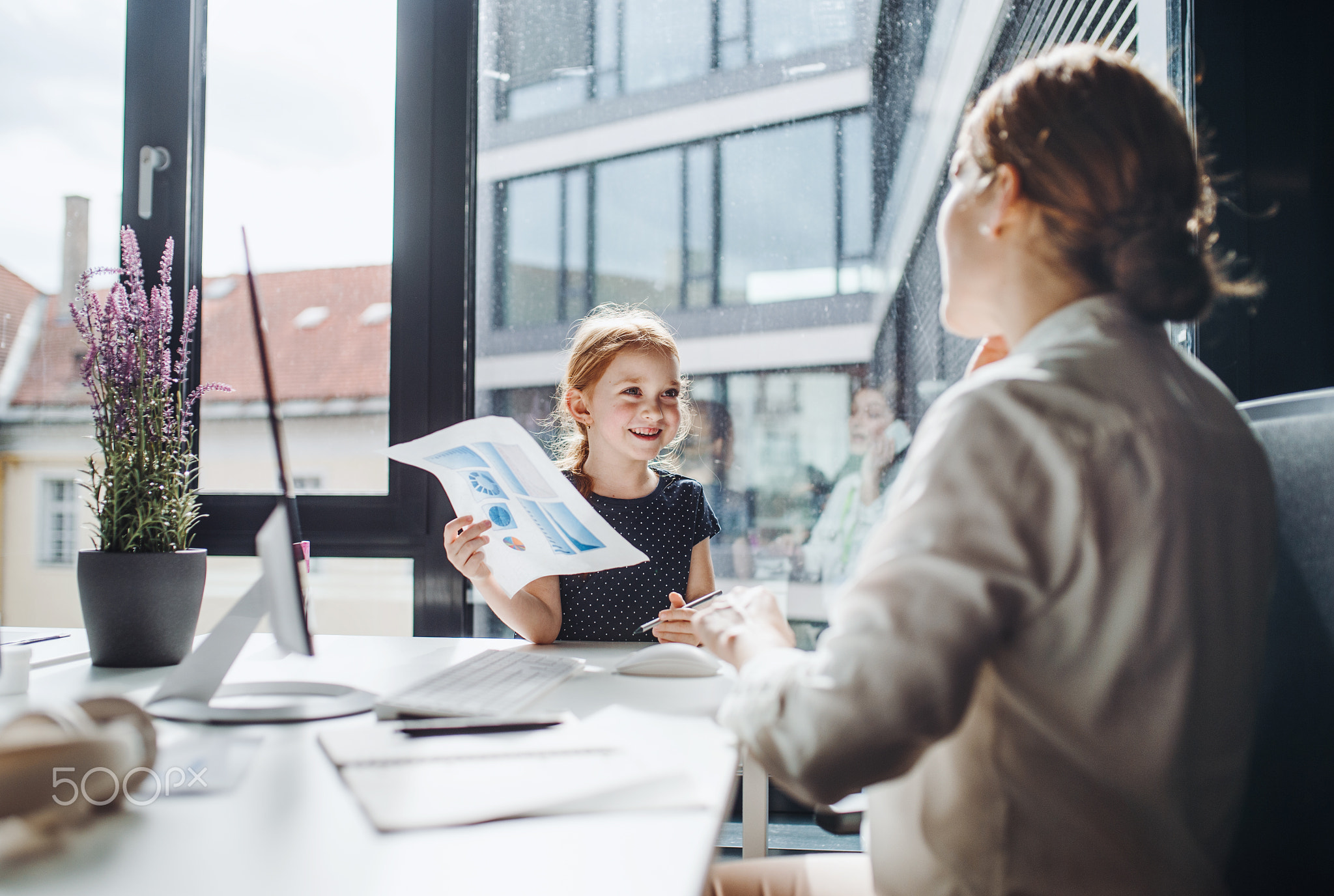 A businesswoman with small daughter sitting in an office, working.