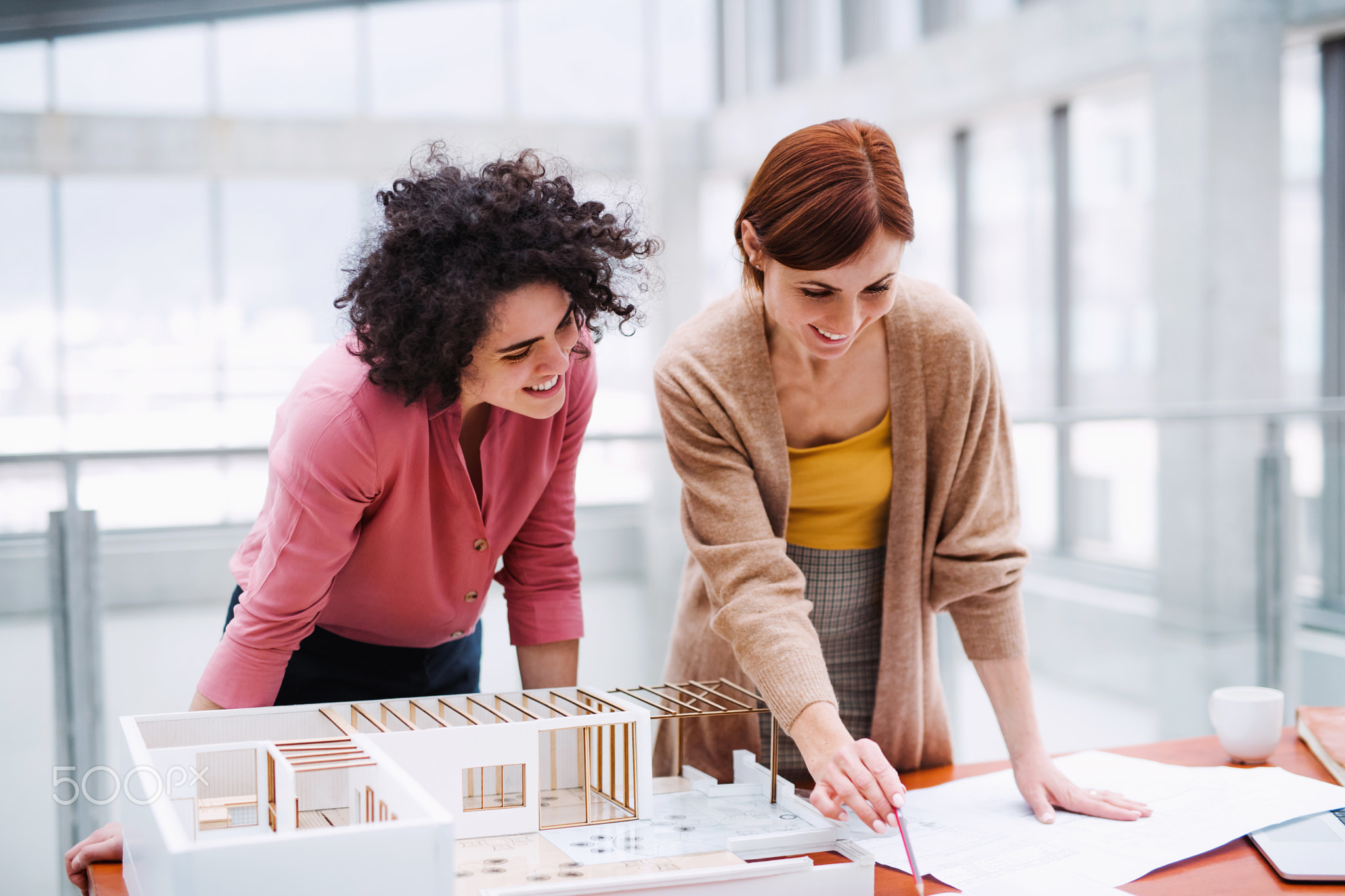 Female young architects with model of a house standing in office, talking.