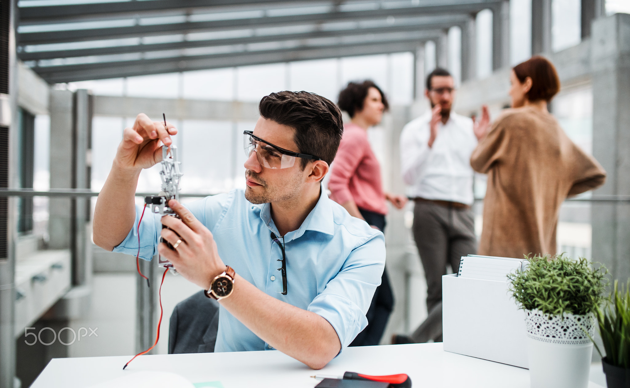 A young businessman or scientist with robotic hand standing in office, working.