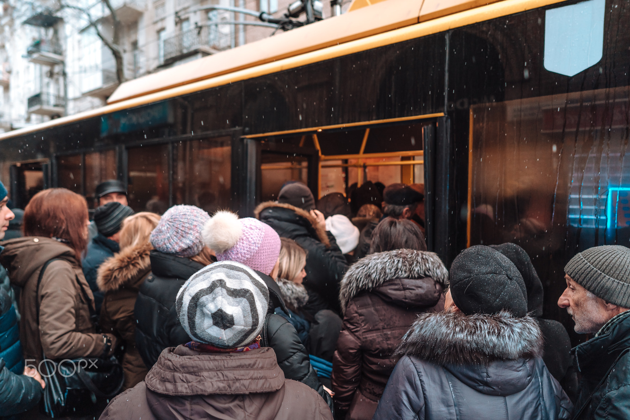 Many unidentified people are waiting for city transport at the bus stop