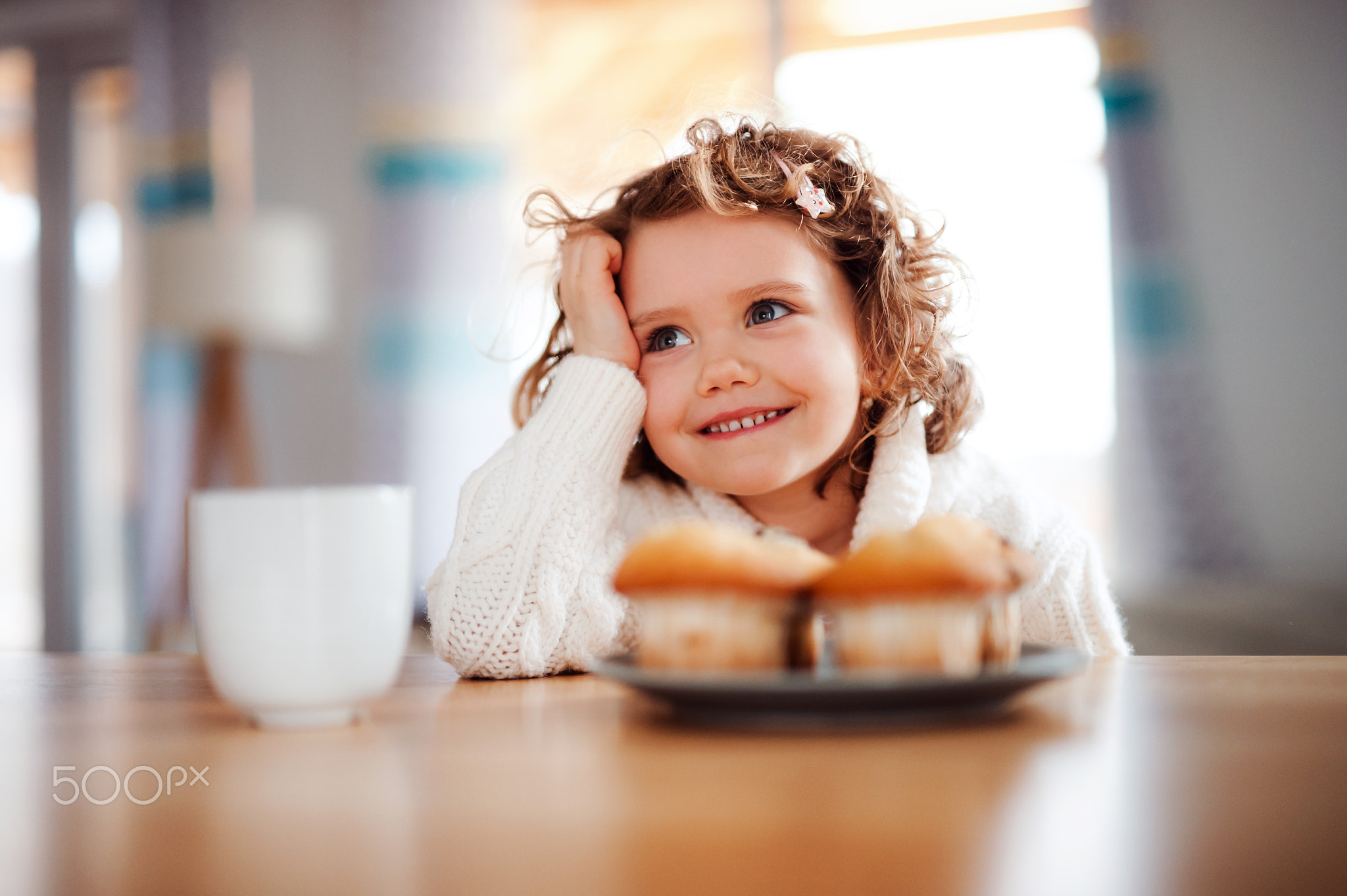 A portrait of small girl with muffins sitting at the table at home.