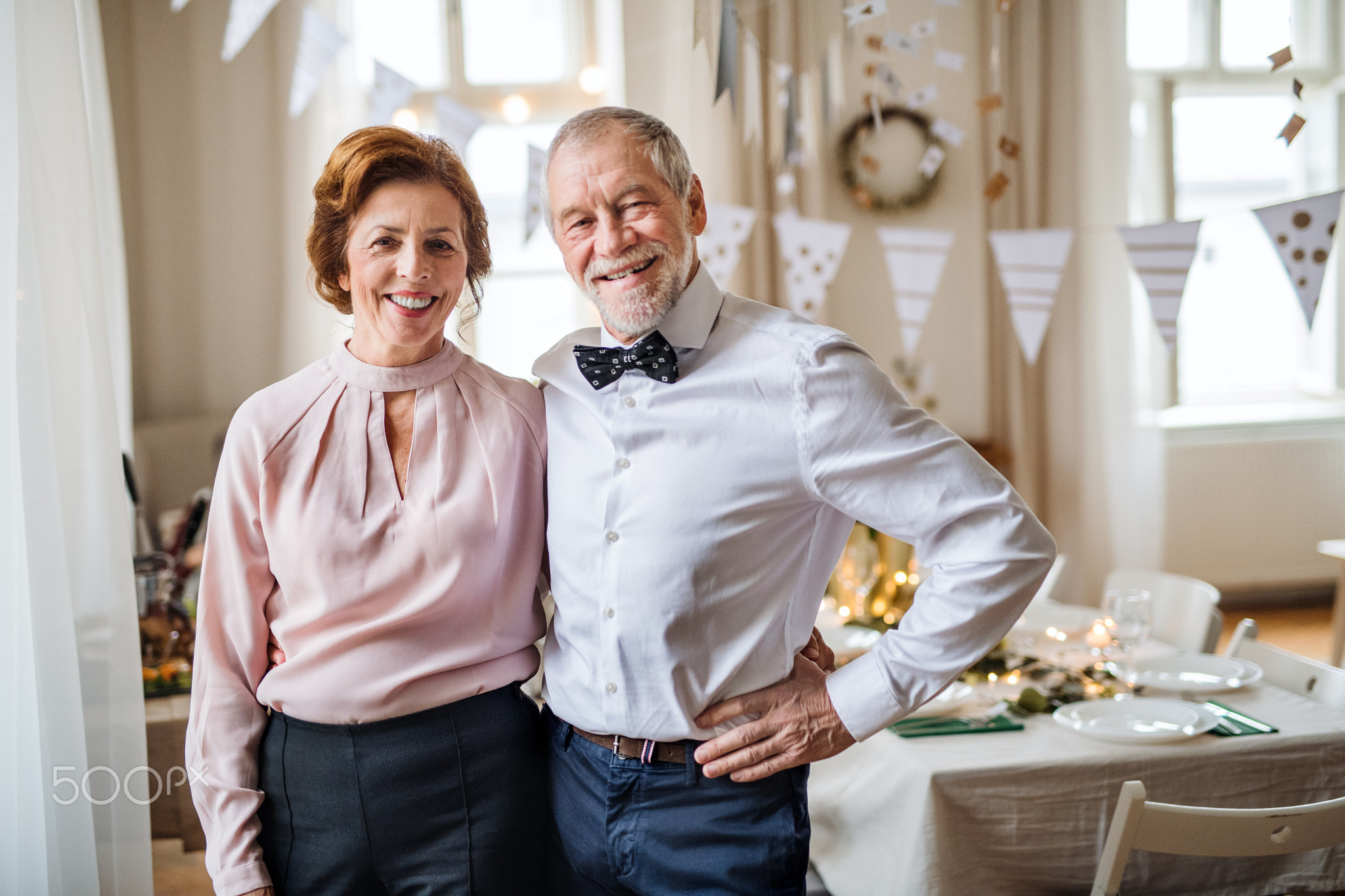 Senior couple standing indoors in a room set for a party. Copy space.