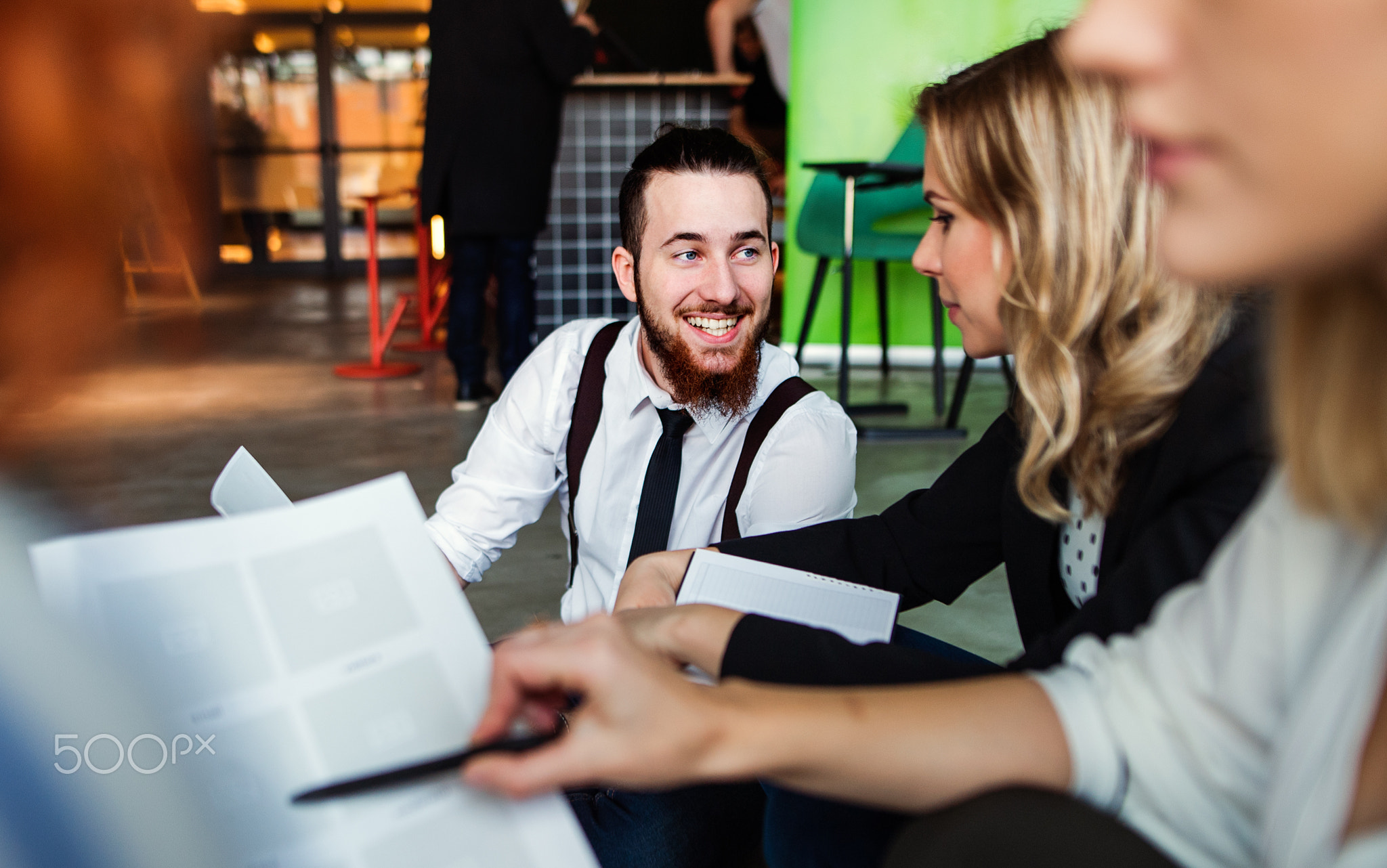 A group of young business people sitting on the floor in an office, talking.