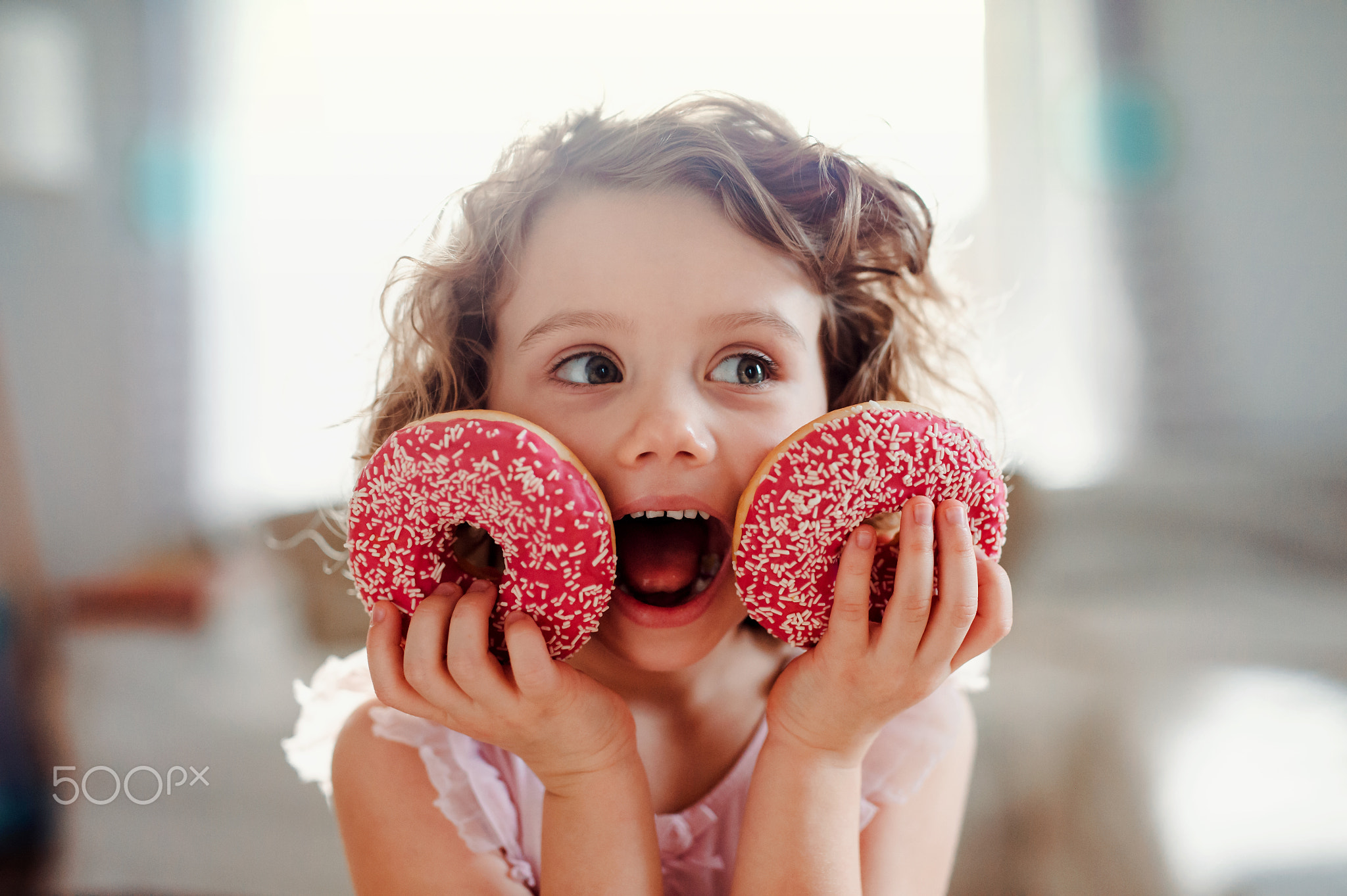 A small girl with doughnuts at home, looking at camera.