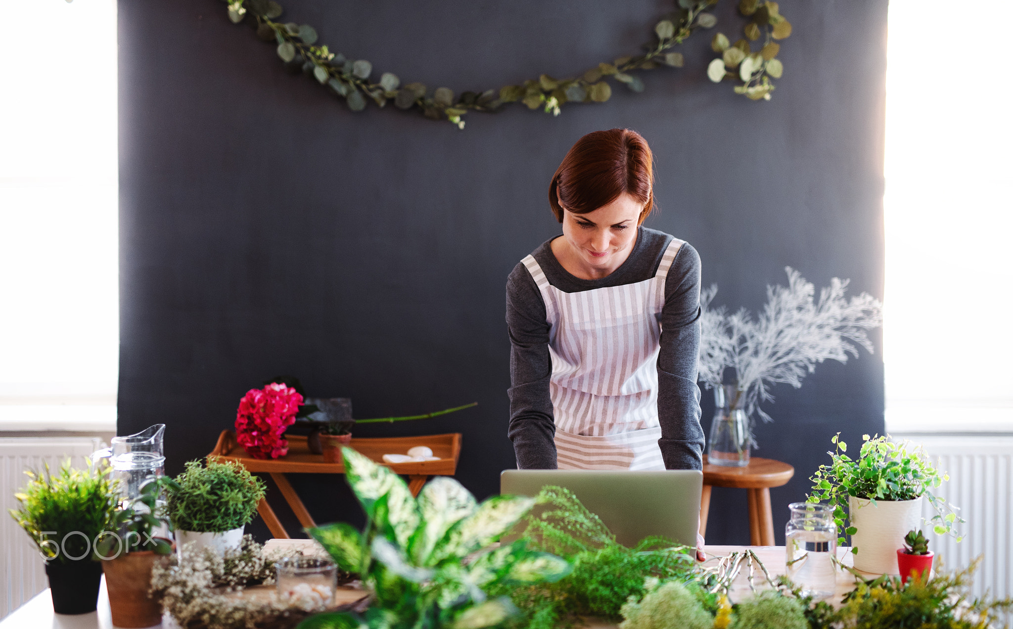 Young creative woman in a flower shop, using laptop. A startup of florist business.