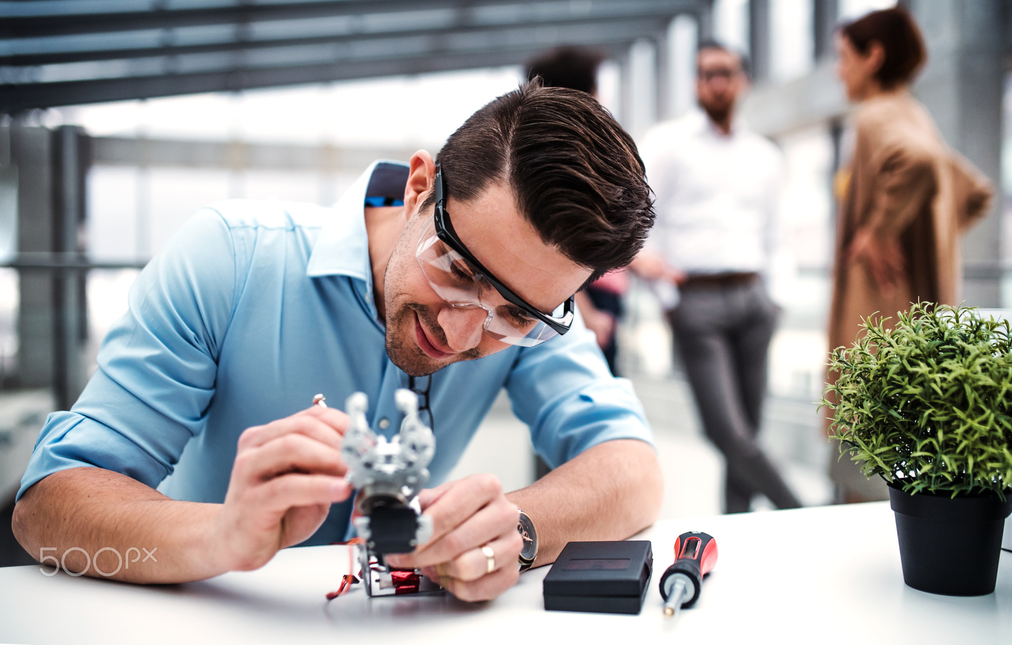 A young businessman or scientist with robotic hand standing in office, working.