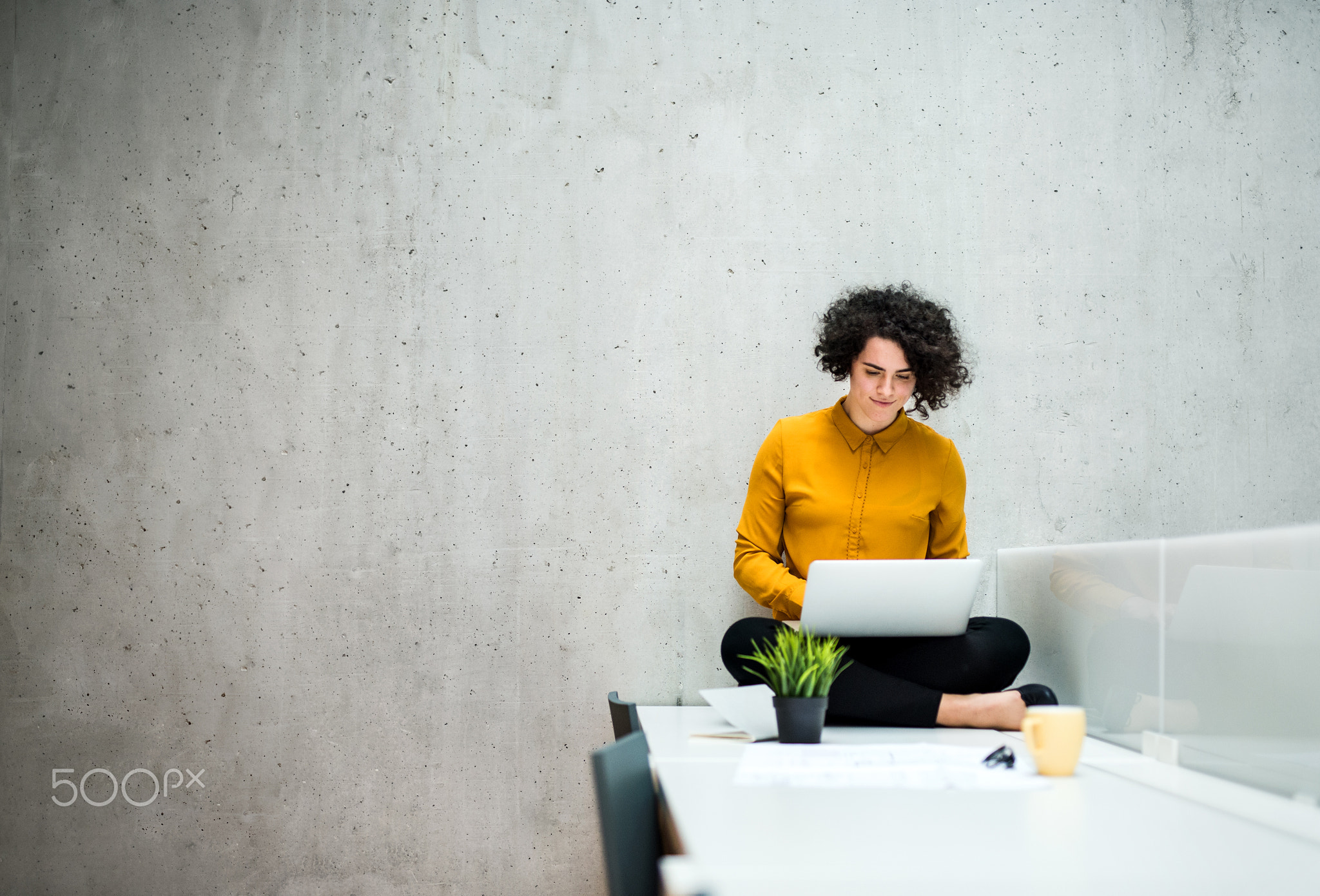 Young student or businesswoman sitting on desk in room in a library or office, using laptop.