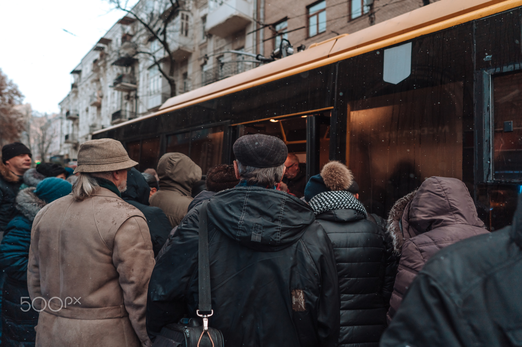 Many unidentified people are waiting for city transport at the bus stop