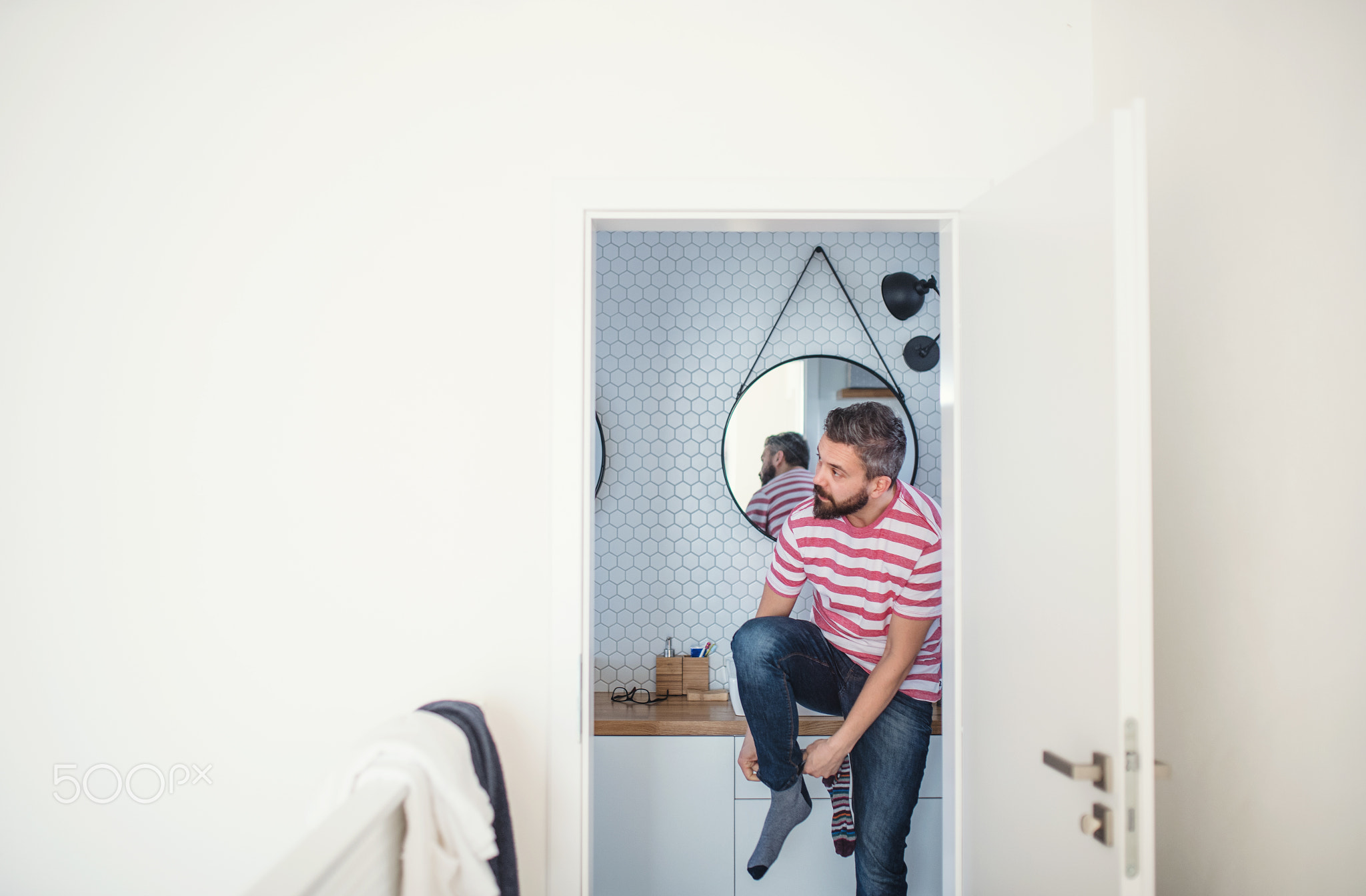 An adult hipster man getting dressed in brahroom indoors at home.