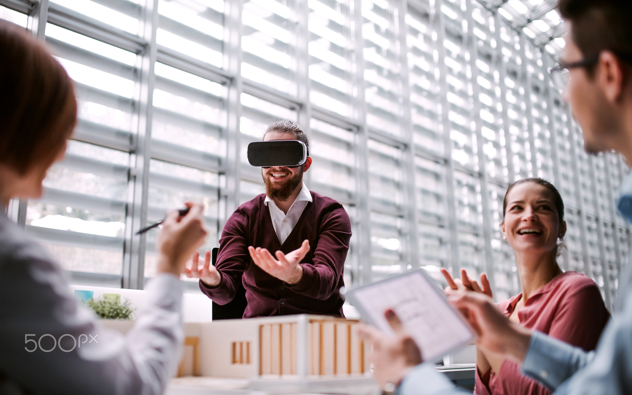 Group of young architects with model of a house and VR goggles working in office.