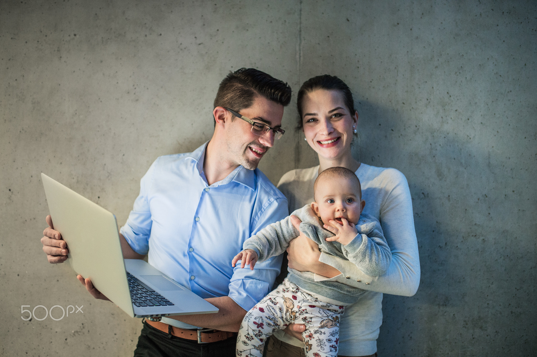 A young businessman with wife and baby daughter standing in office, using laptop.