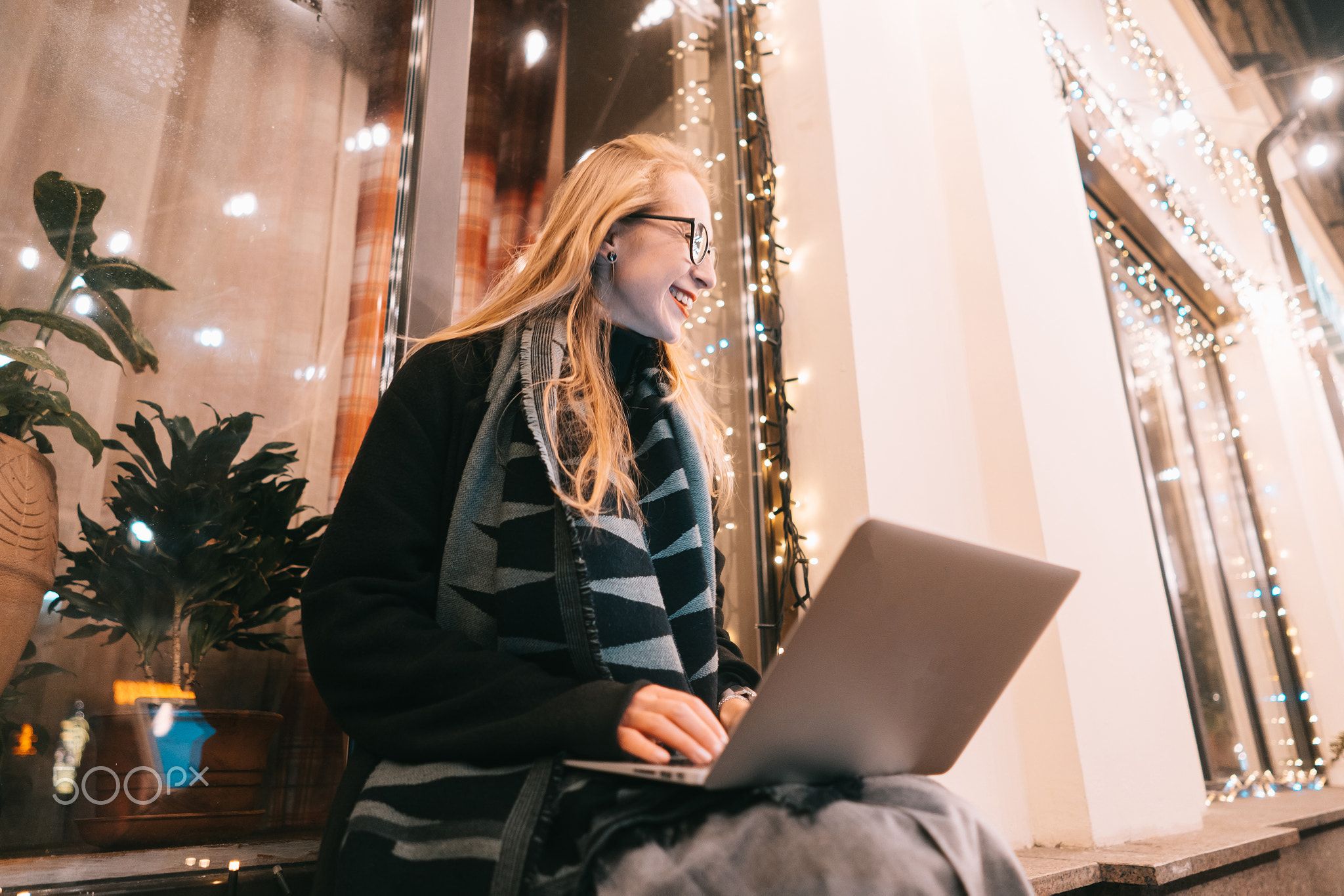 side view of young woman using laptop on street with night city