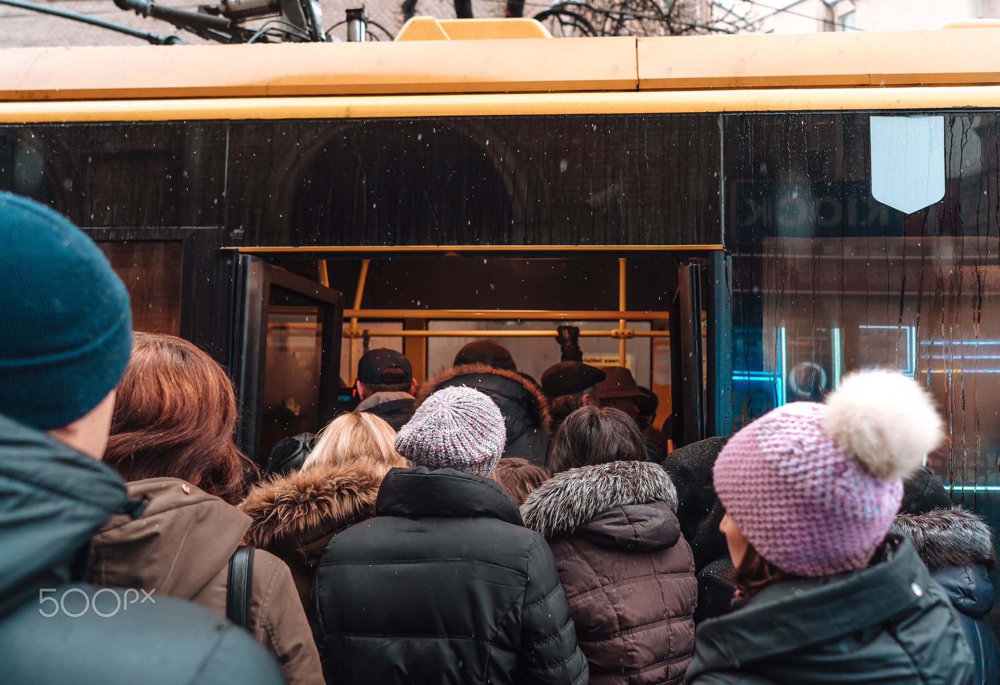 Many unidentified people are waiting for city transport at the bus stop