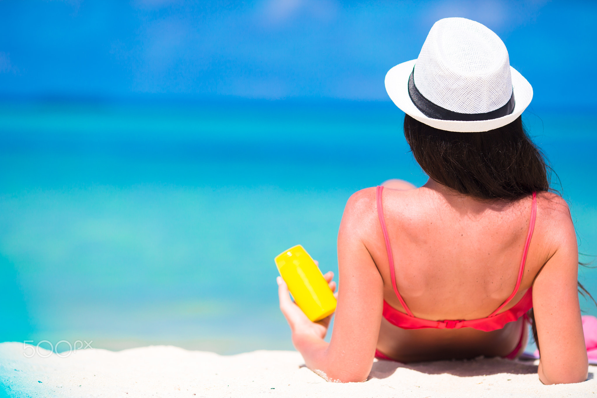 Beautiful young woman holding a suncream lying on tropical beach
