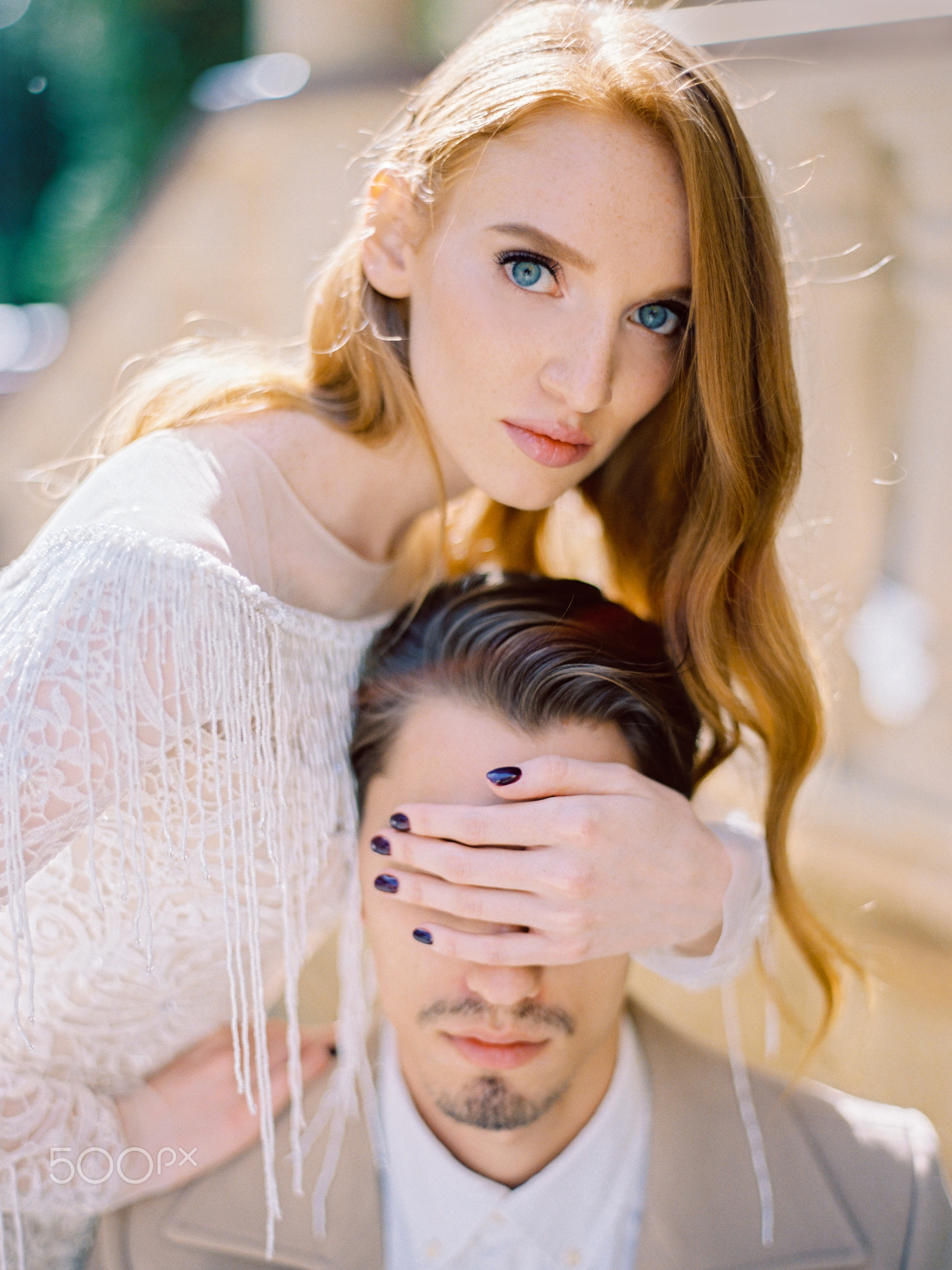 Red-haired bride closes the eyes of a man groom wi