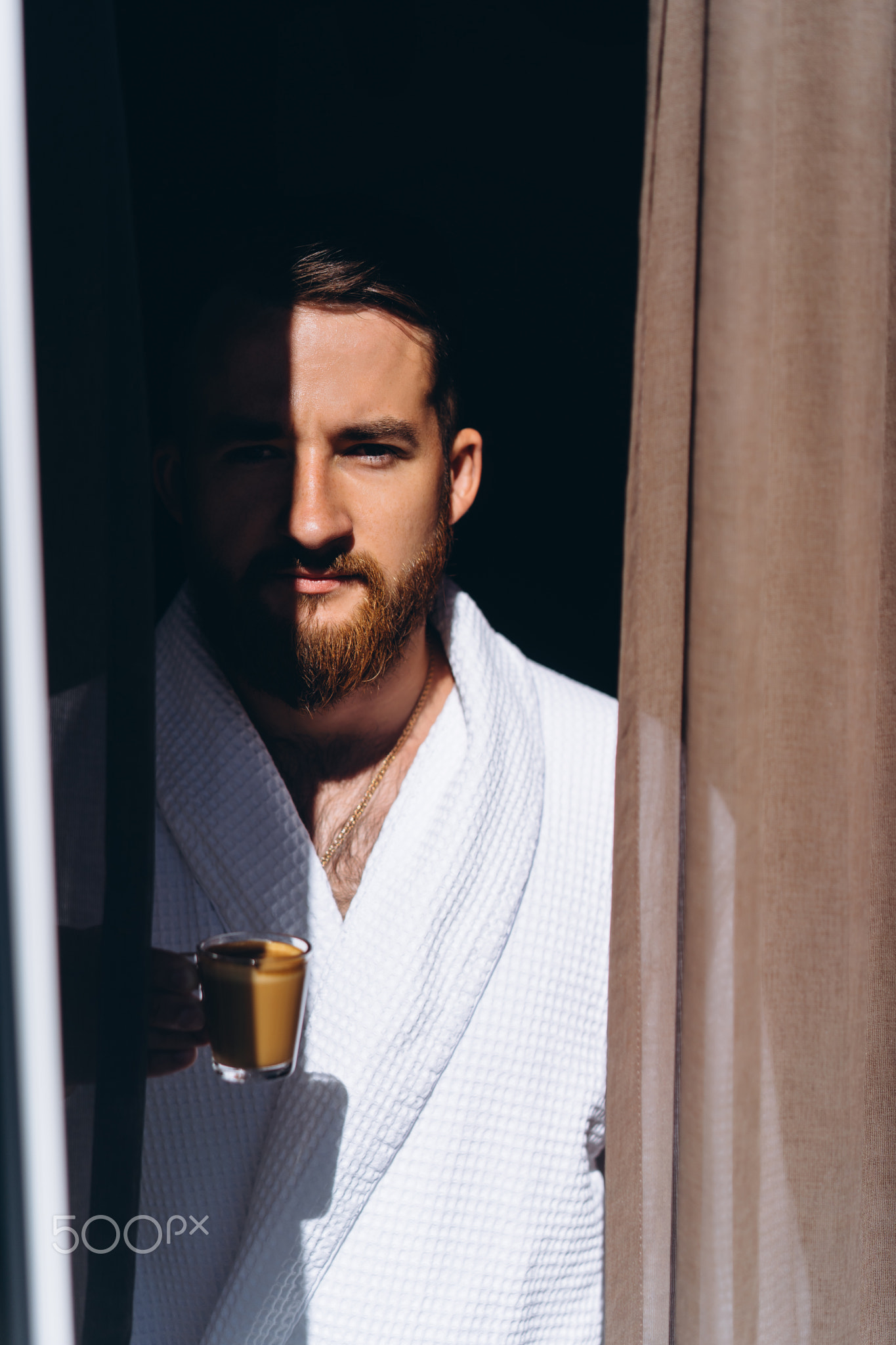 Male in white bathrobe with coffee mug in hand.