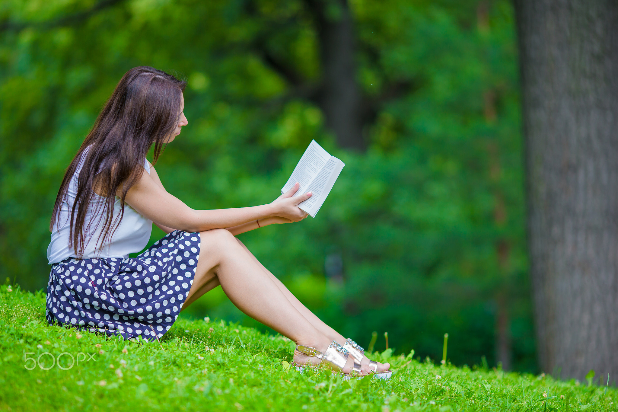 Young girl reading a book outside in park