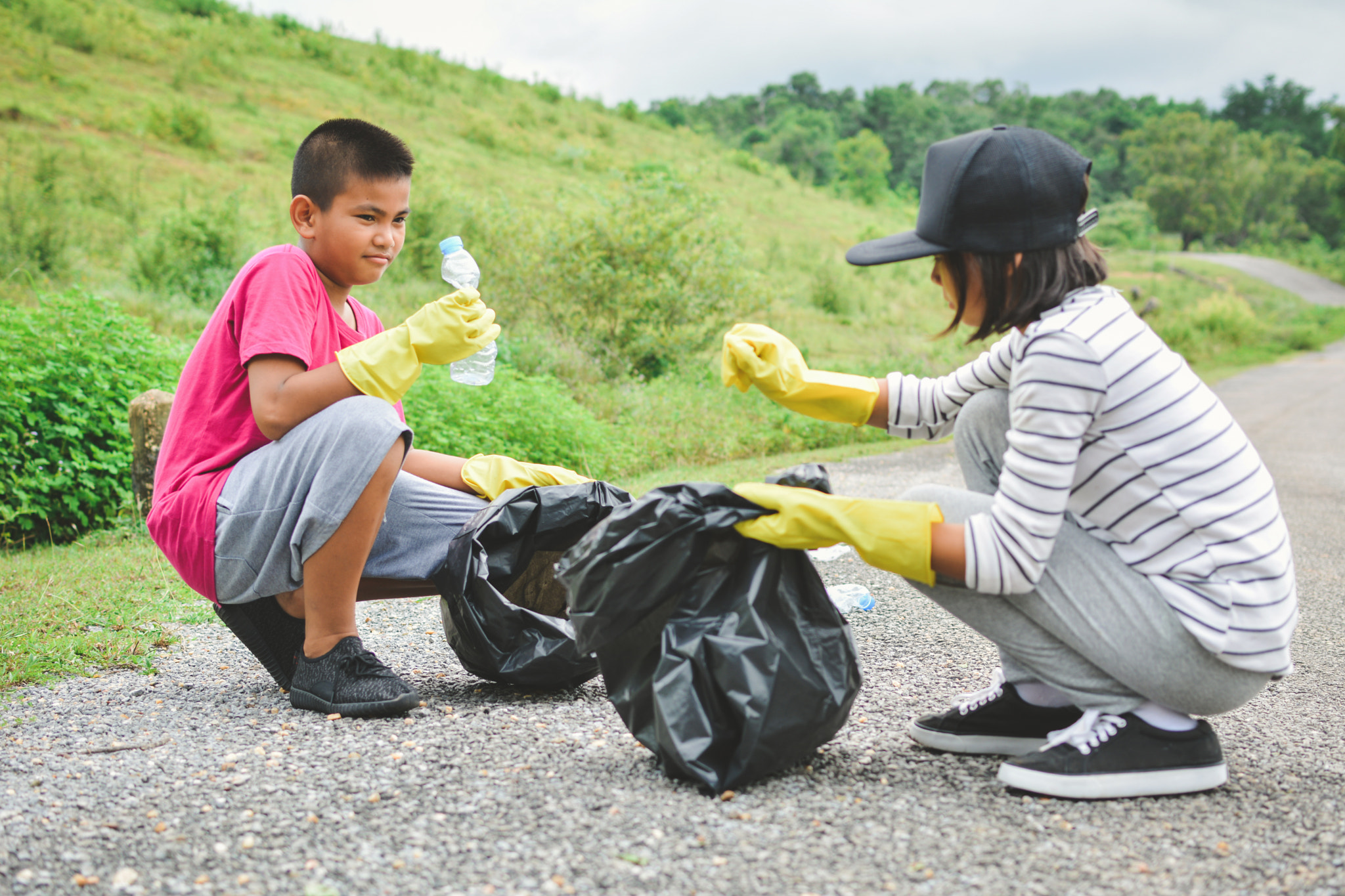 Children hands in yellow gloves picking up empty of bottle plast