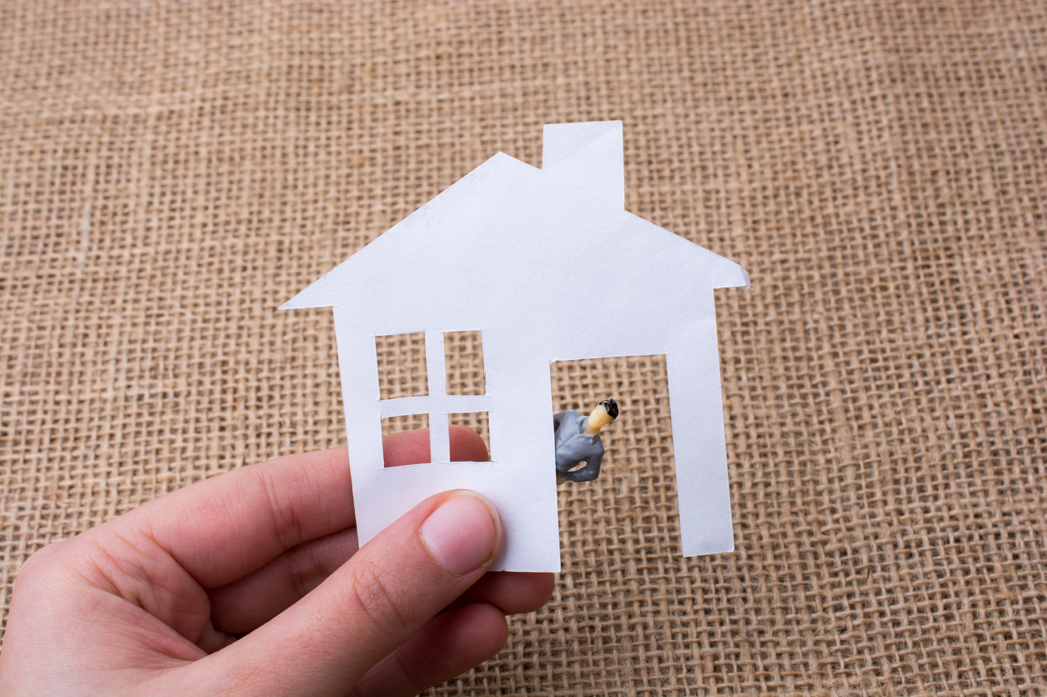 Paper house and a man figurine on a canvas background