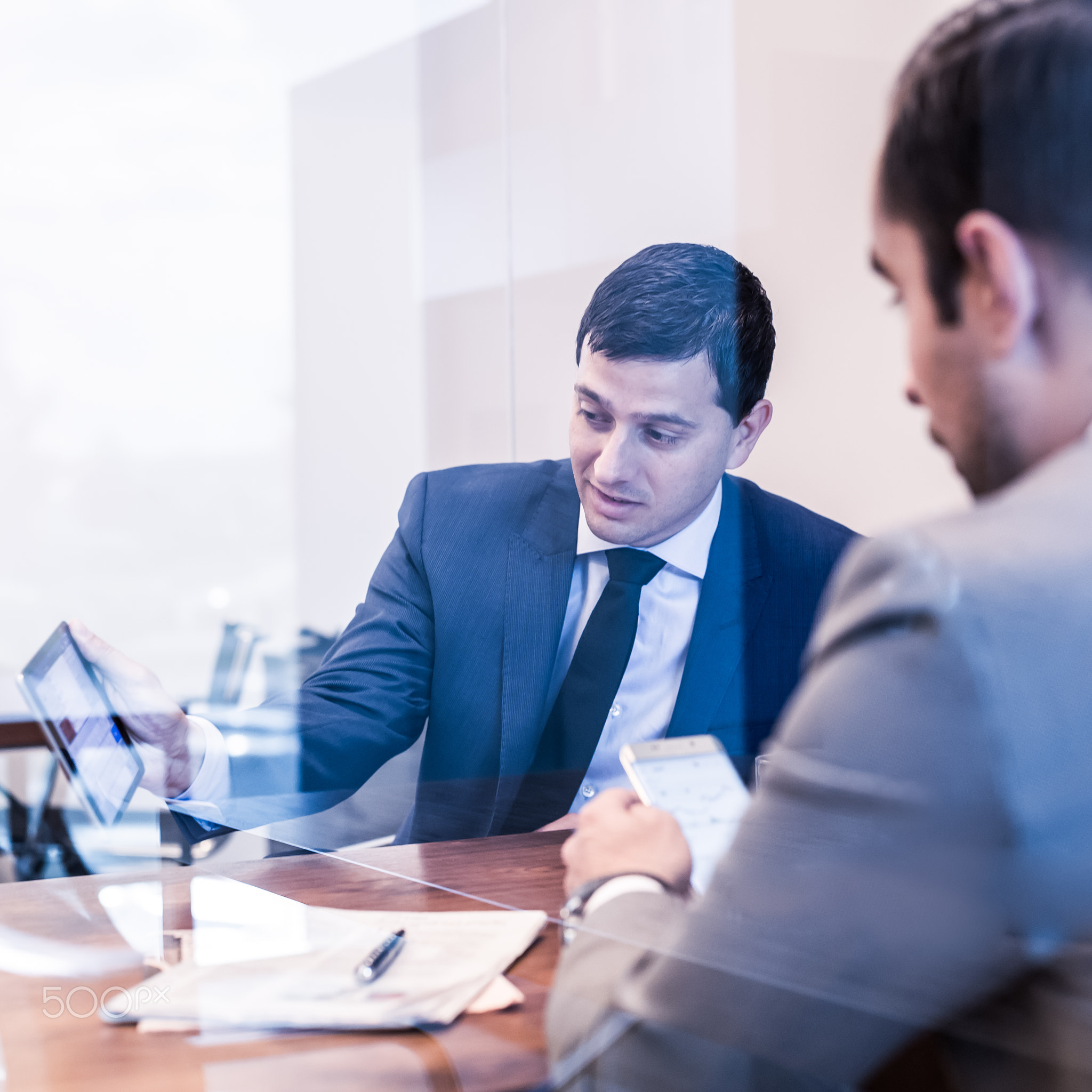 Two young businessmen using electronic devices at business meeting.