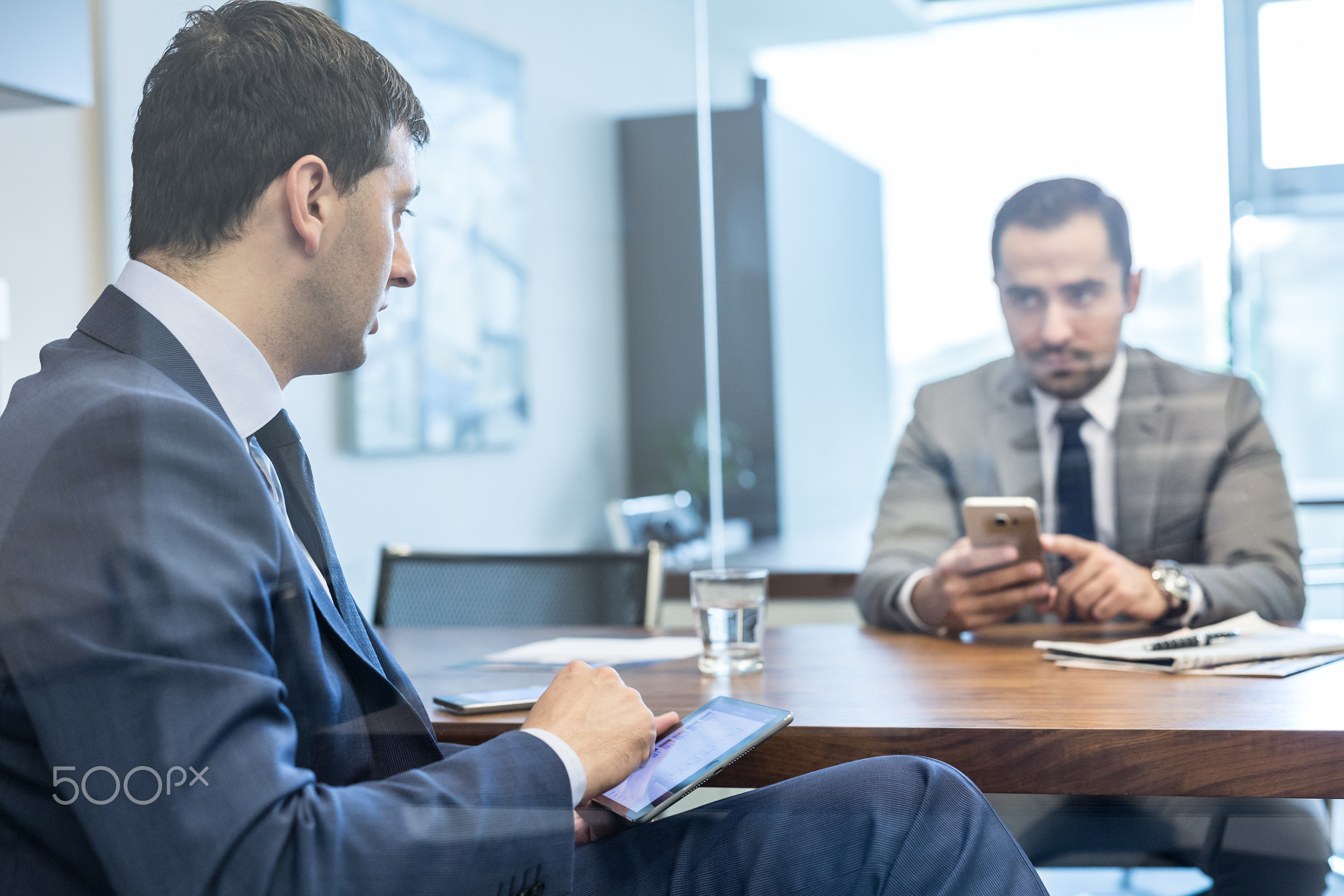 Two young businessmen using electronic devices at business meeting.