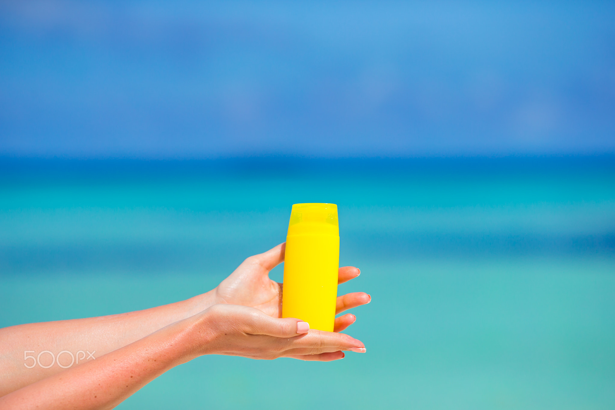 Female hands with suncream bottle background blue sea