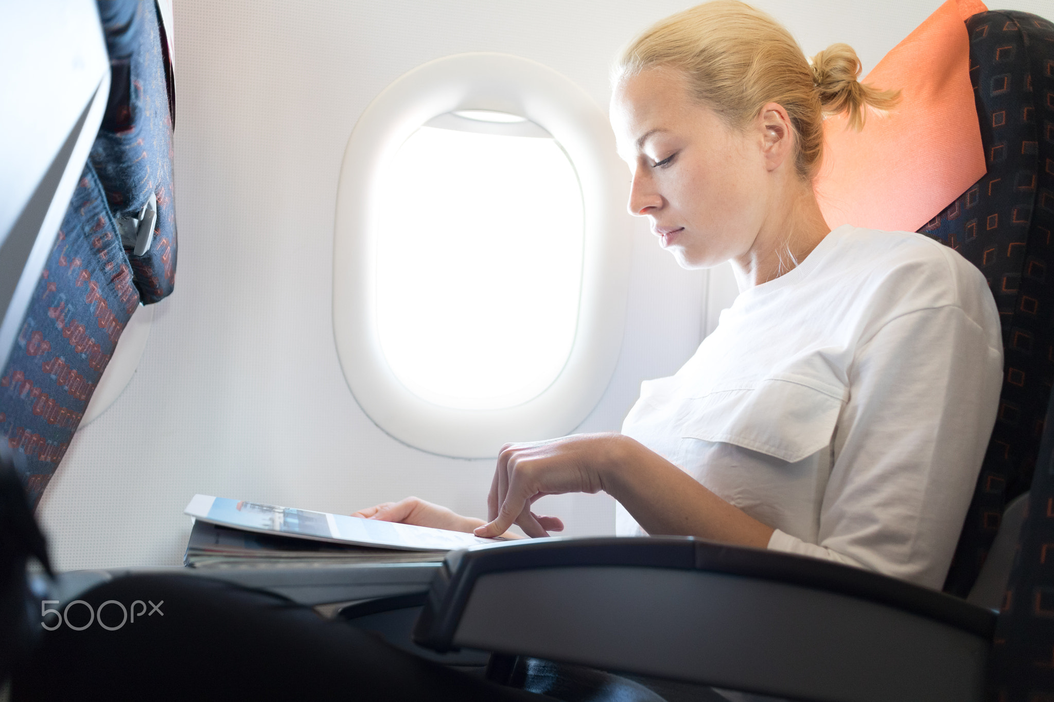 Woman reading in flight magazine on airplane. Female traveler reading seated in passanger cabin....