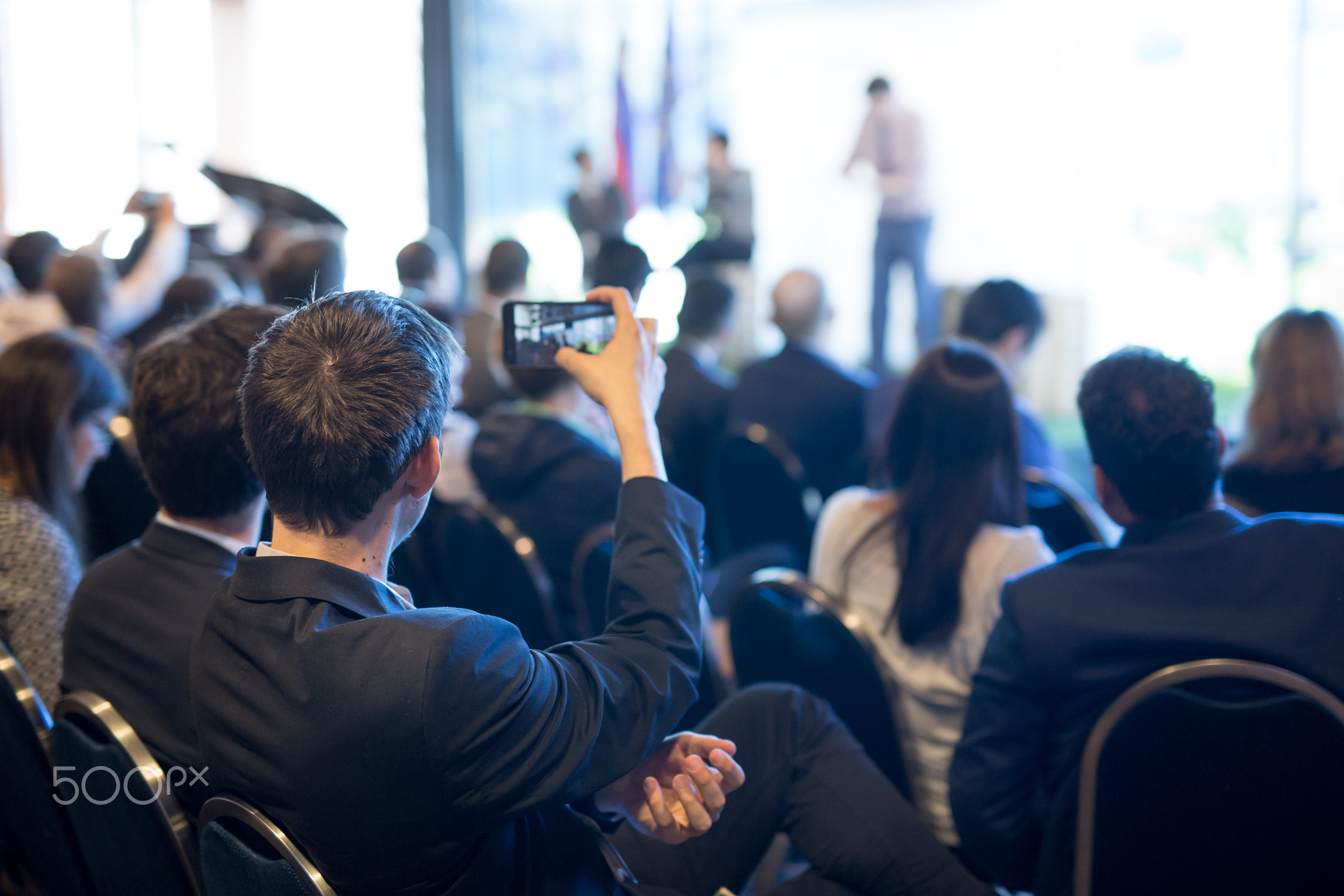 Businessman takes a picture of corporate business presentation at conference hall using smartphone.