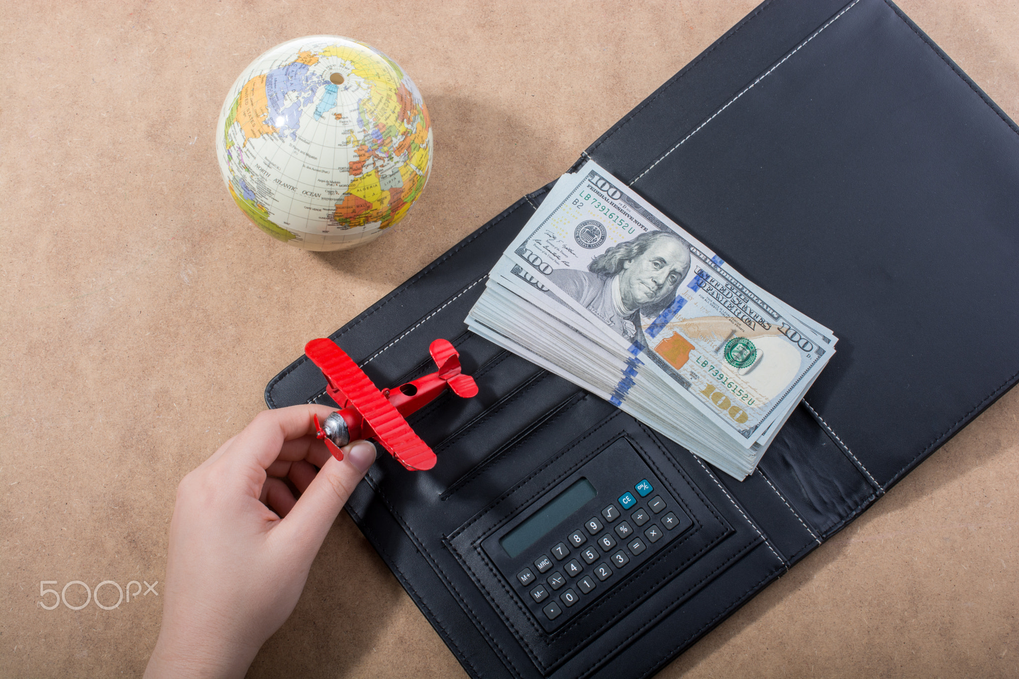 Hand holding model airplane beside globe and dollars