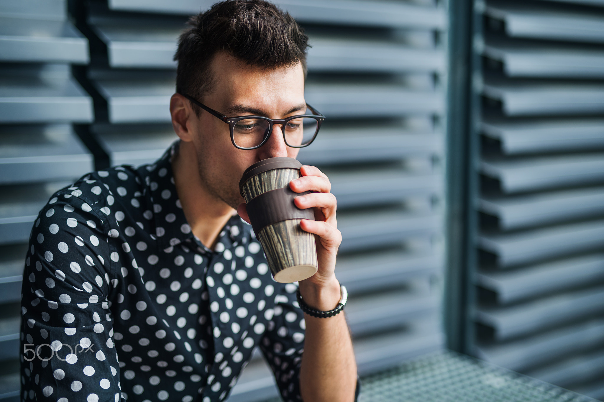 A young businessman sitting outdoors, drinking coffee.