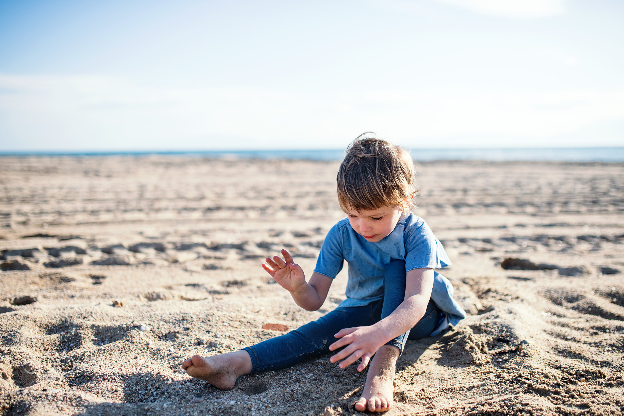 A small girl playing in sand outdoors on beach.