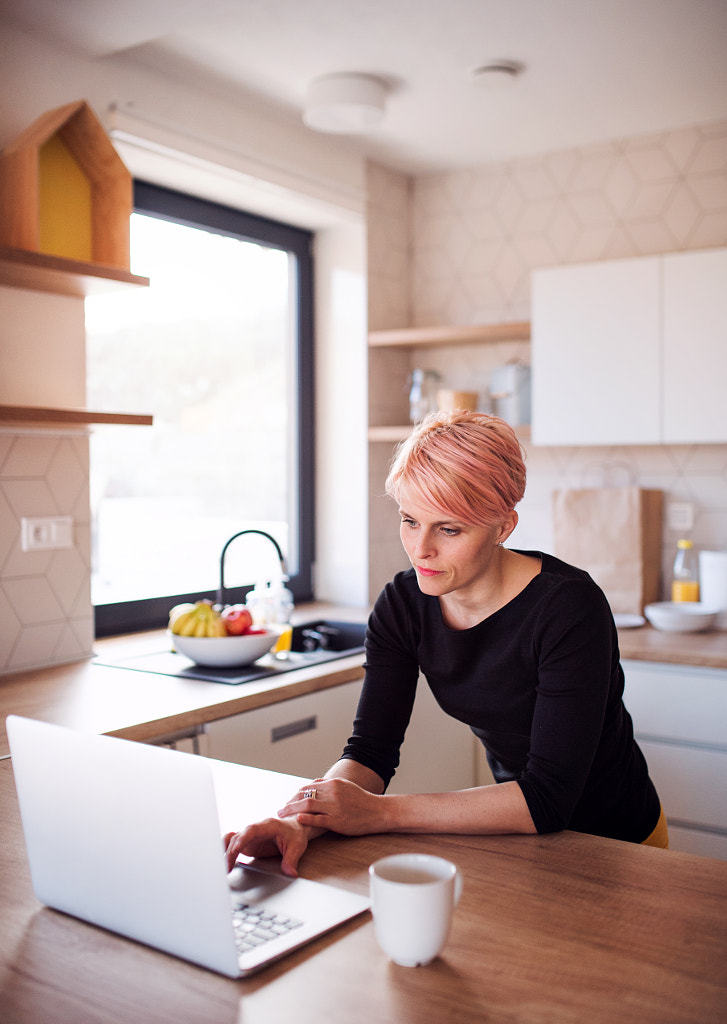 A young woman using laptop in a kitchen at home. by Jozef Polc on 500px.com