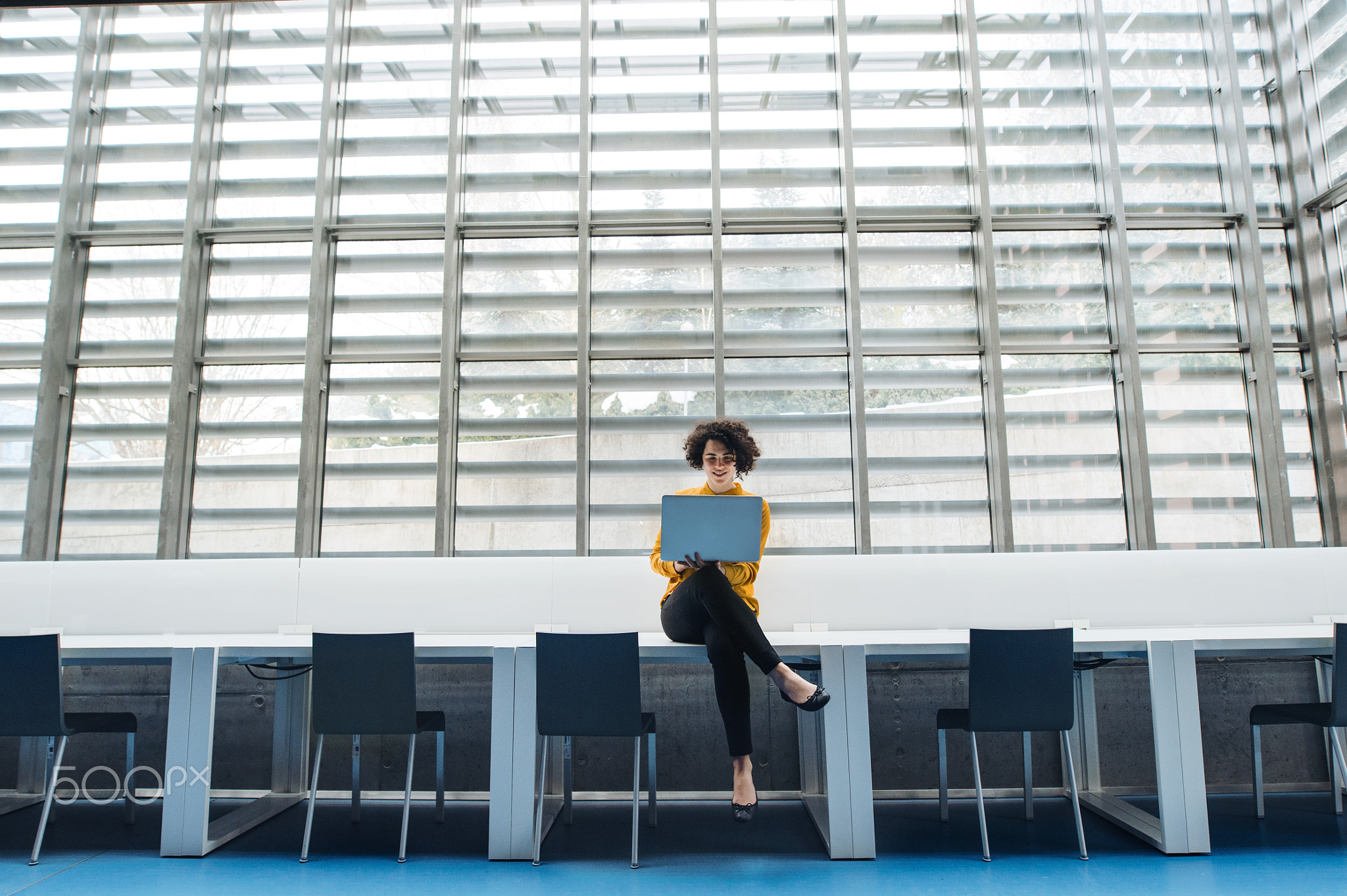 Young student or businesswoman sitting on desk in room in a library or office, using laptop.